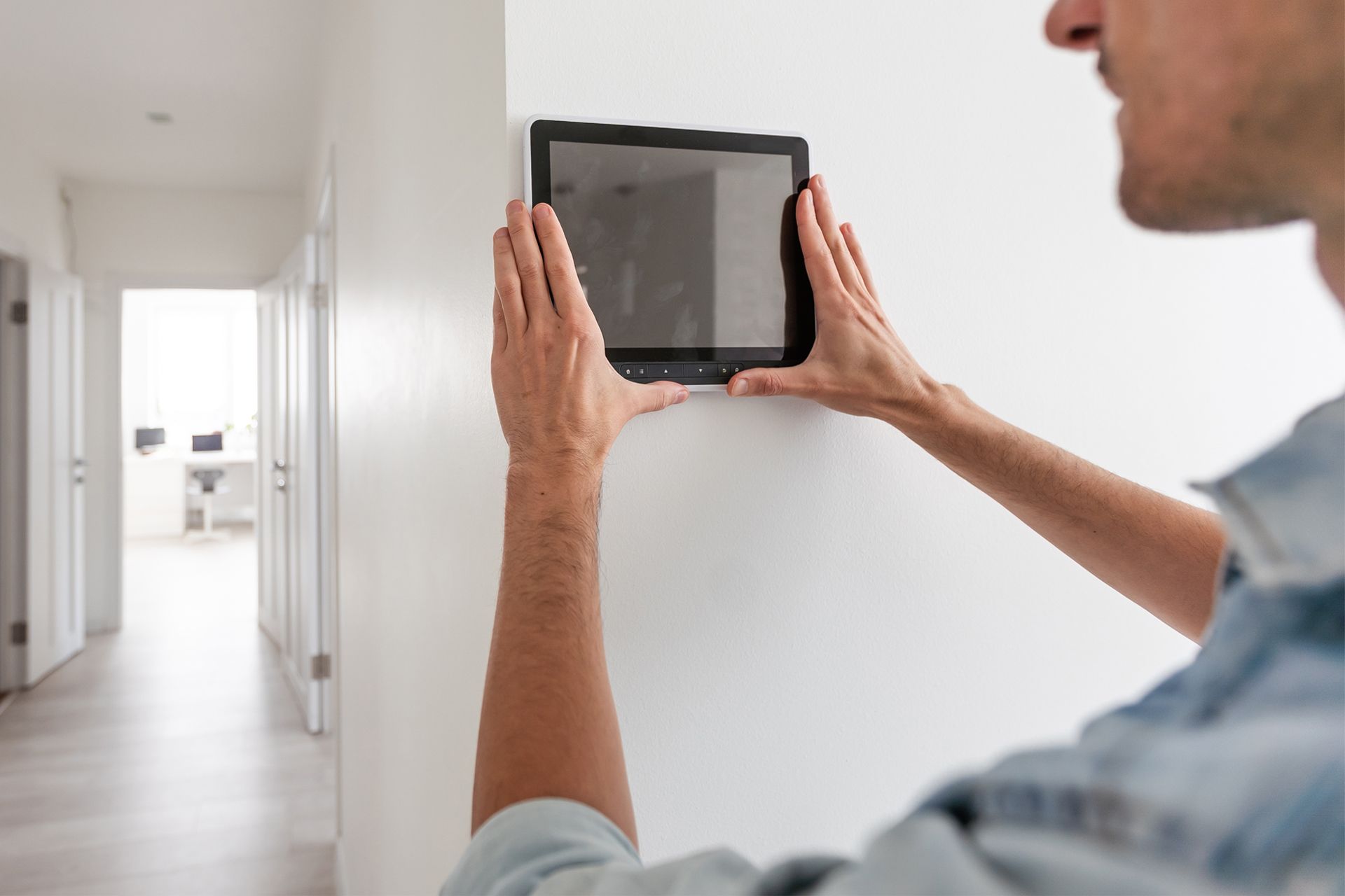 Person measuring a wall with a tablet in a bright, empty hallway,