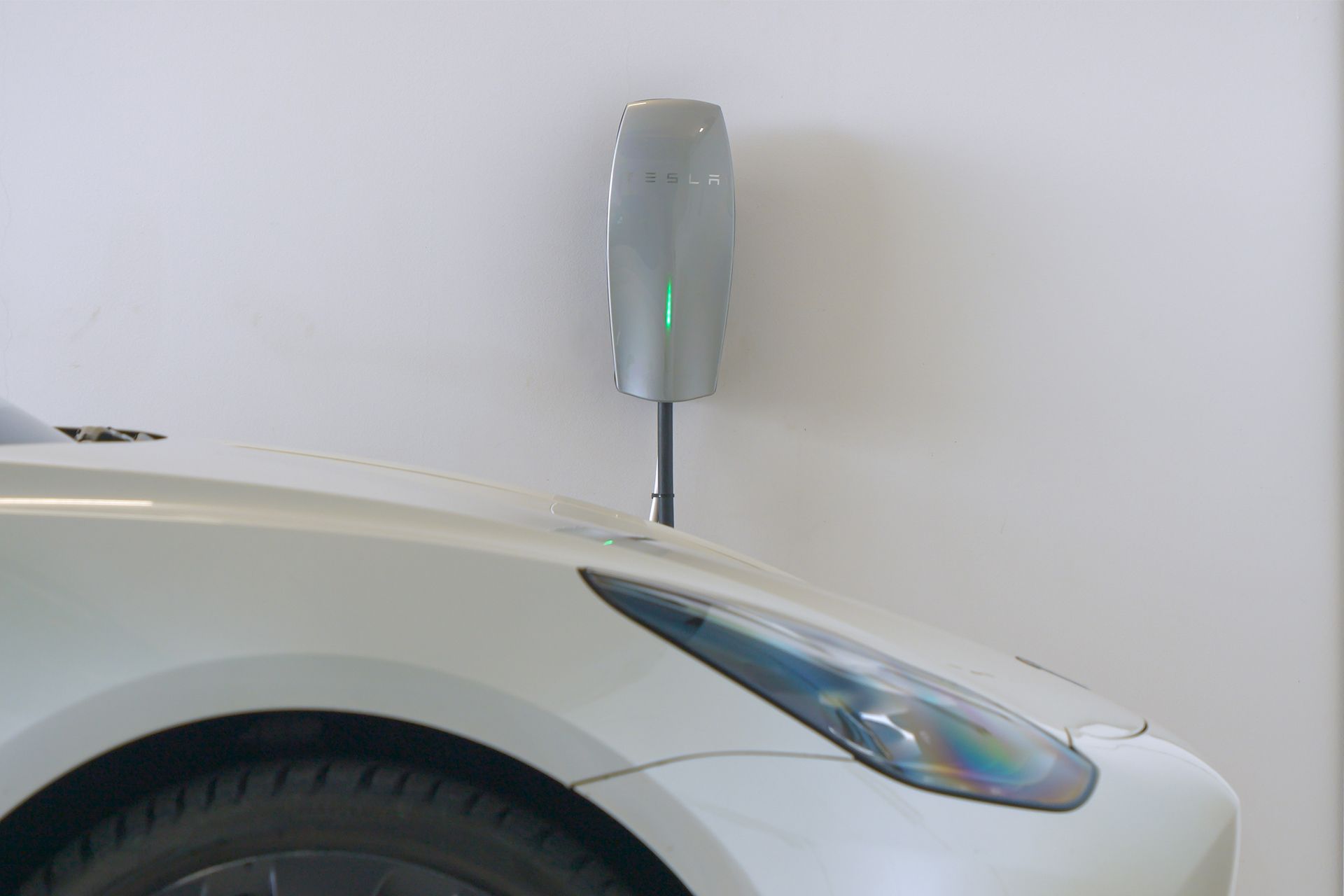 White car charging beside a gray wall-mounted EV charger.