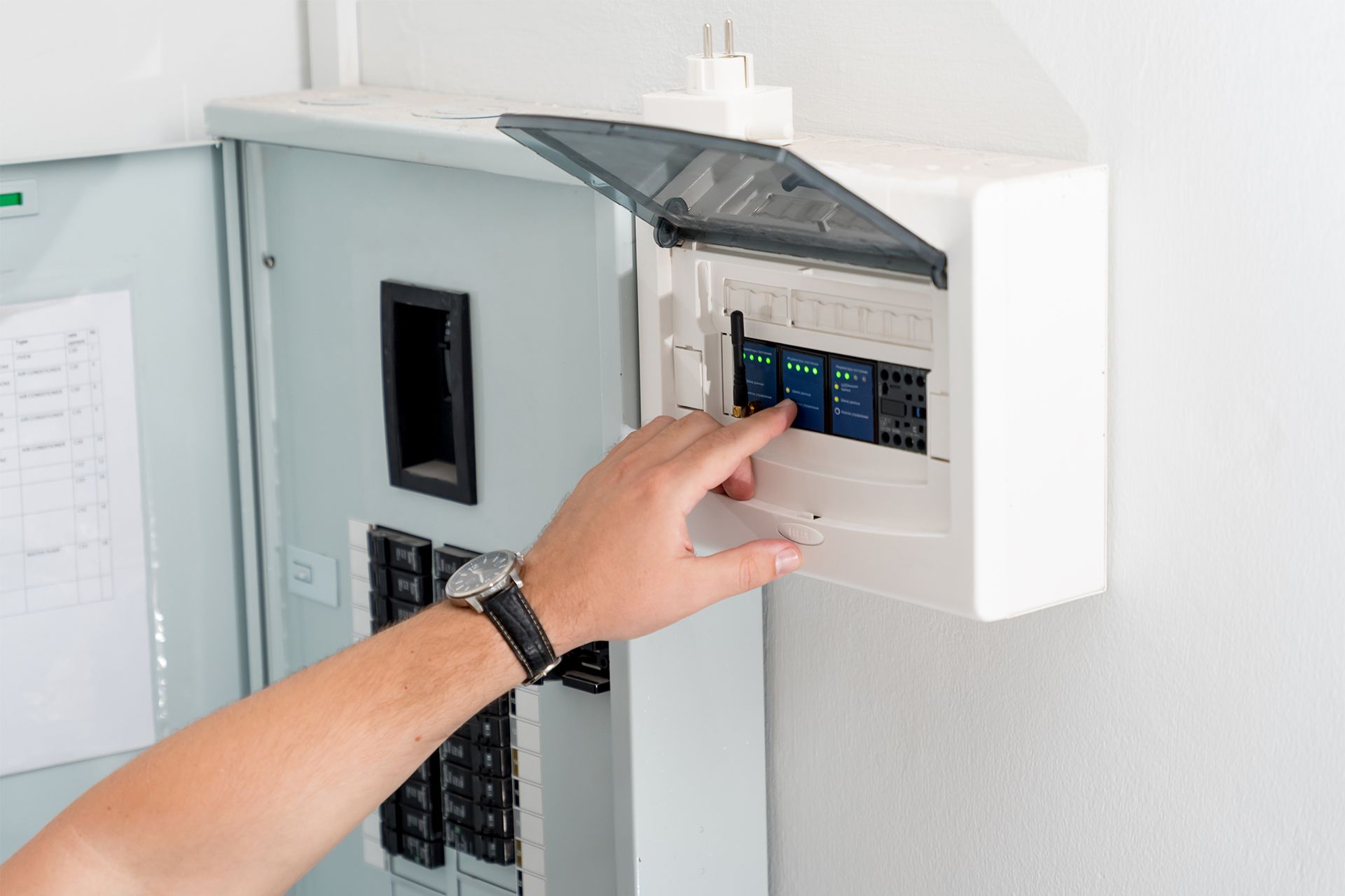 Hand turning breaker switch on an open electrical panel in a white wall box.