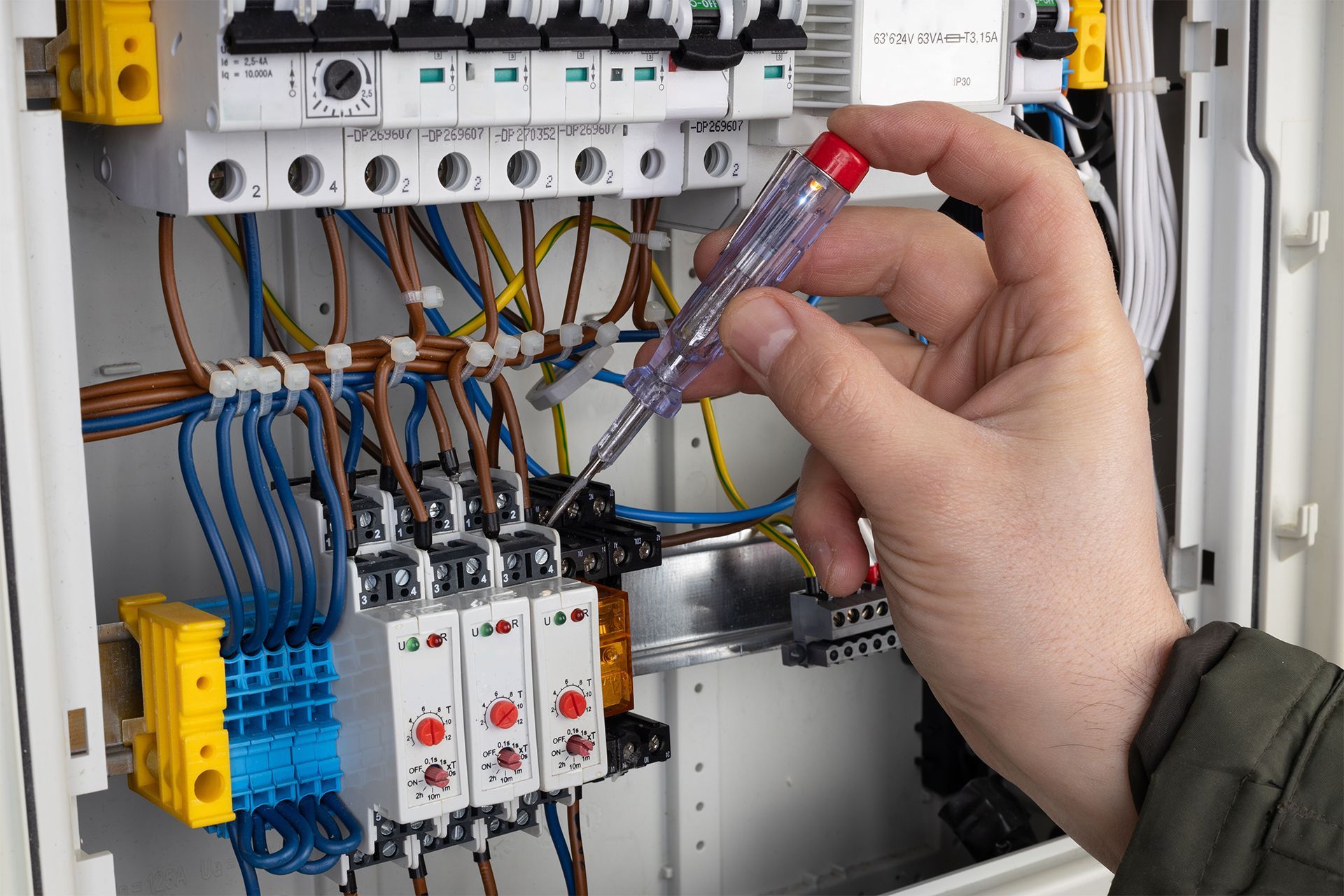 Hand testing wires inside an electrical control panel with circuit breakers and relays.