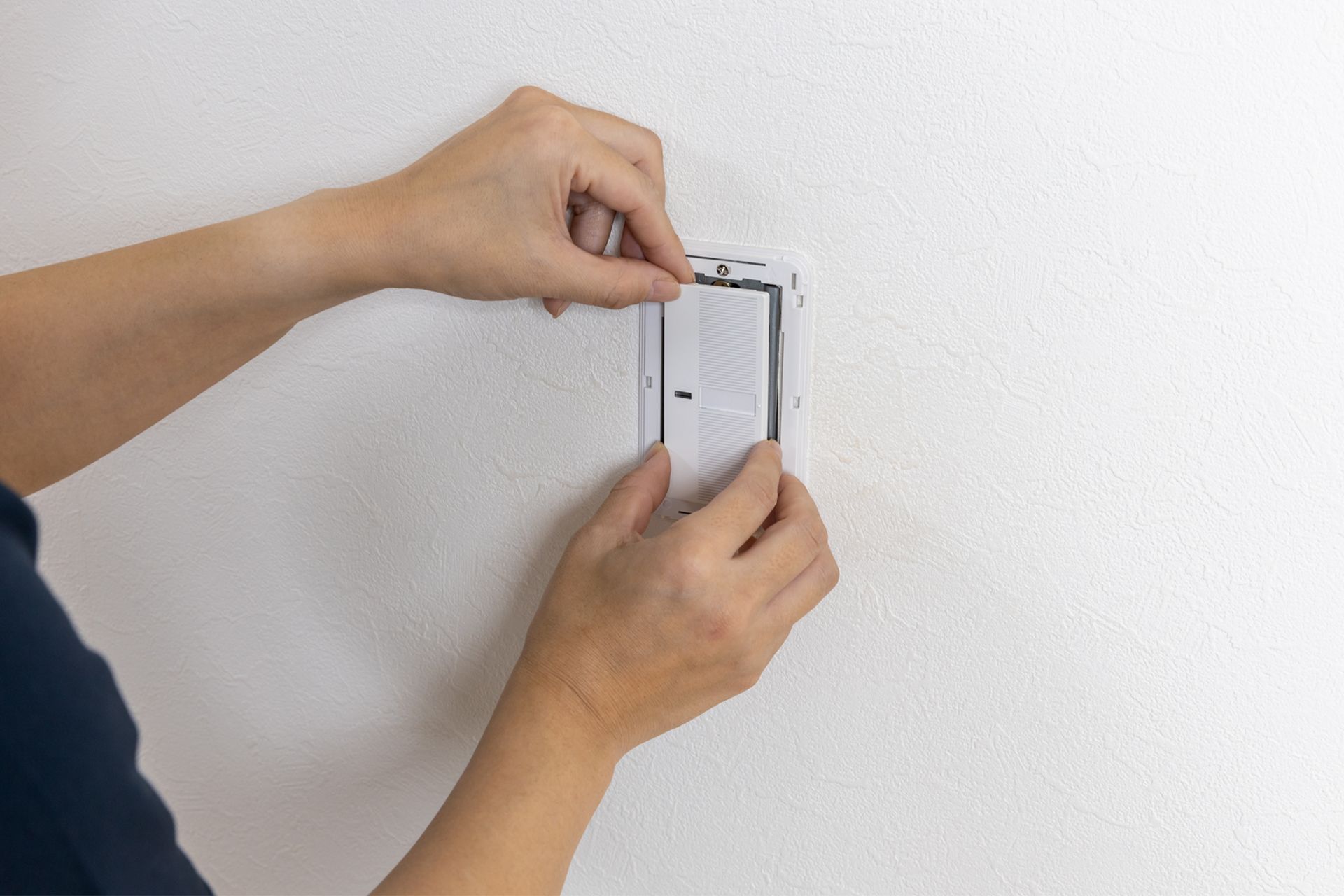 Hands mounting a white wall plate on a light-colored wall.