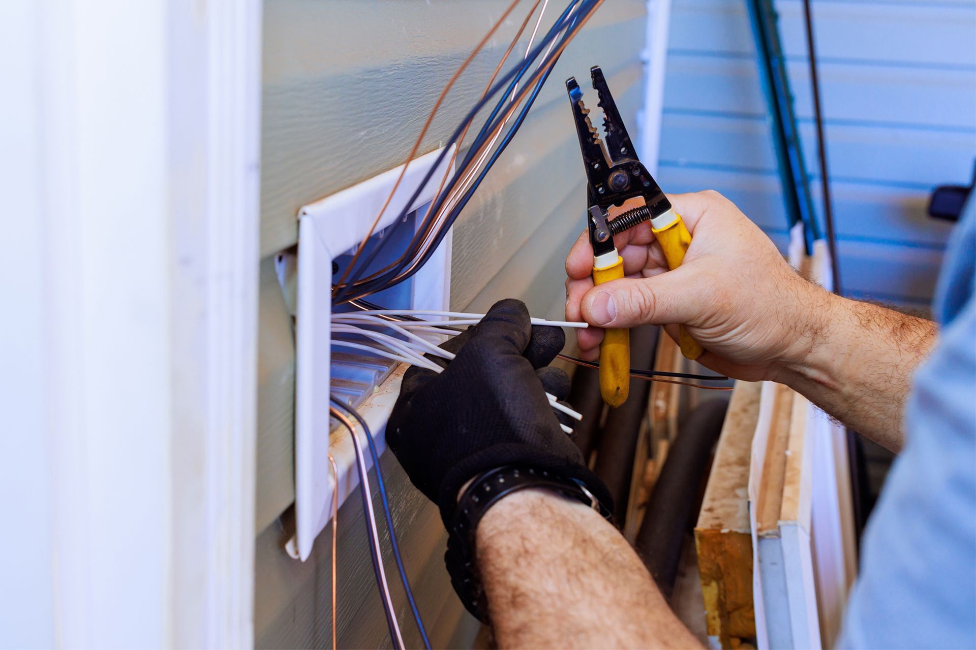 Technician wiring an electrical panel with pliers and gloved hands inside a wall box.
