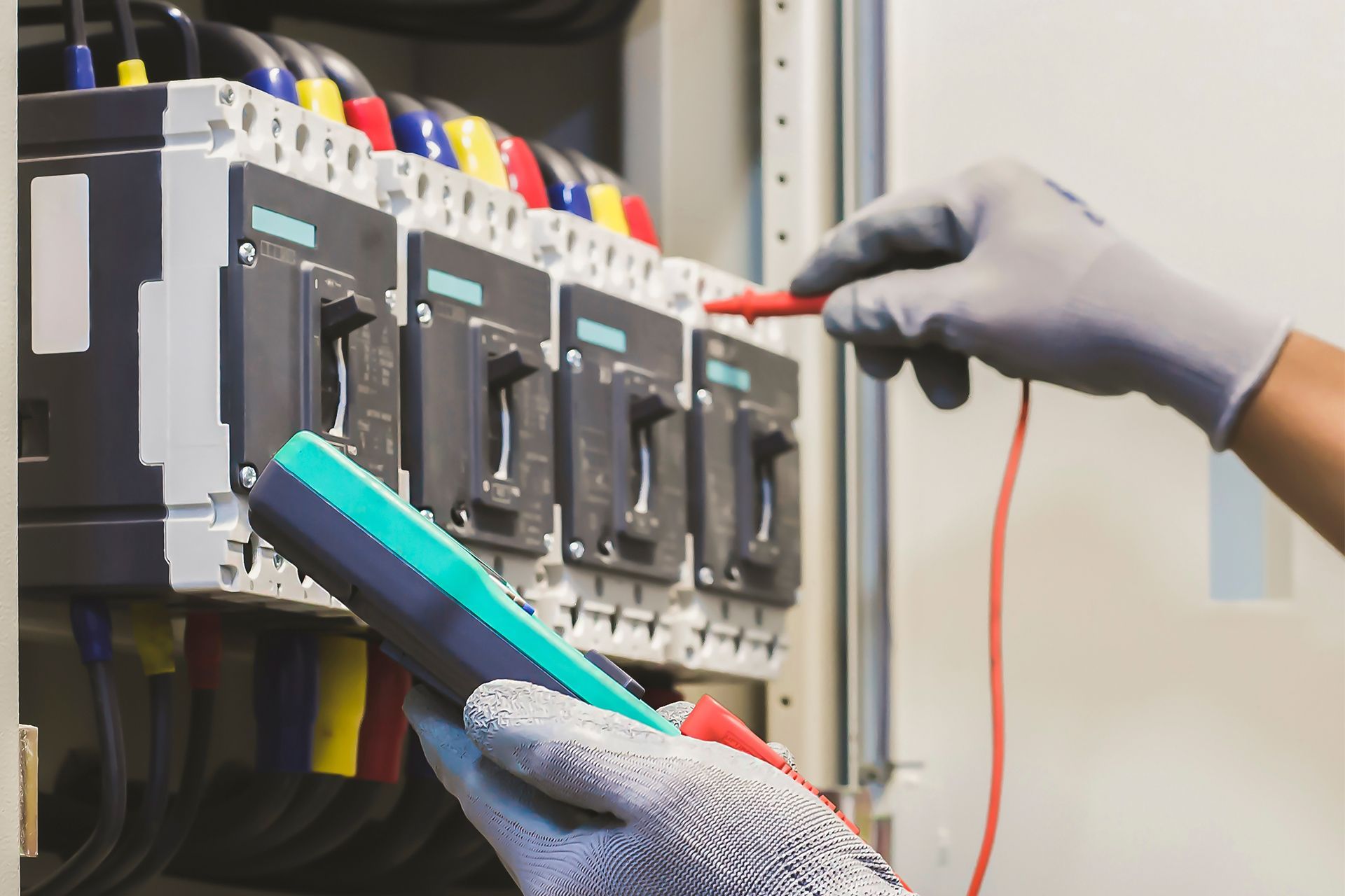Gloved hands testing electrical breakers in a panel with a multimeter probe.