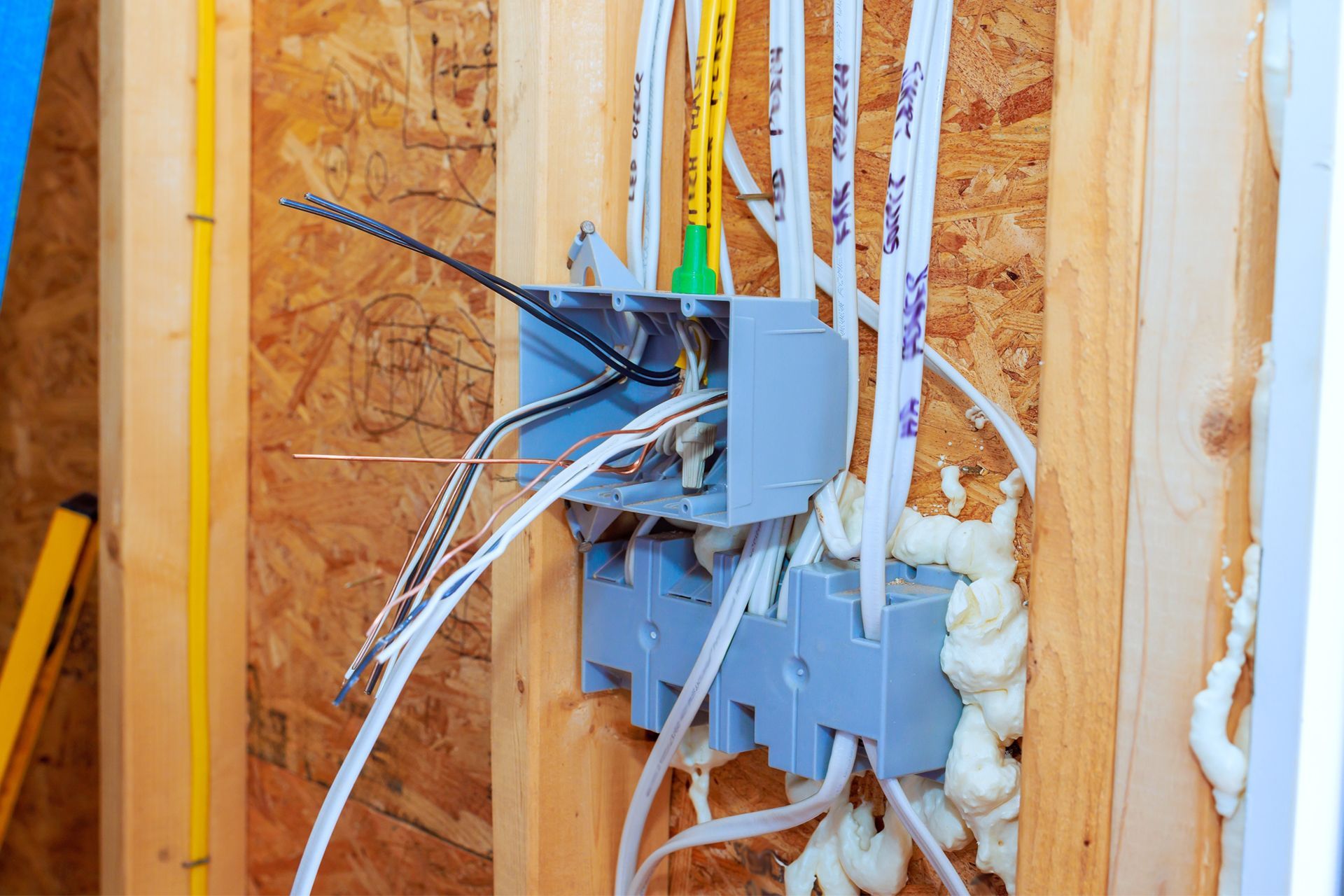 Electrical wiring and outlet boxes exposed in an unfinished wooden wall with spray foam insulation.