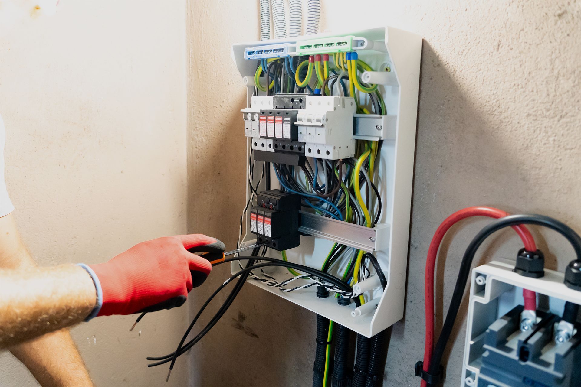Gloved hand testing wires inside an open electrical control panel with multicolored cables