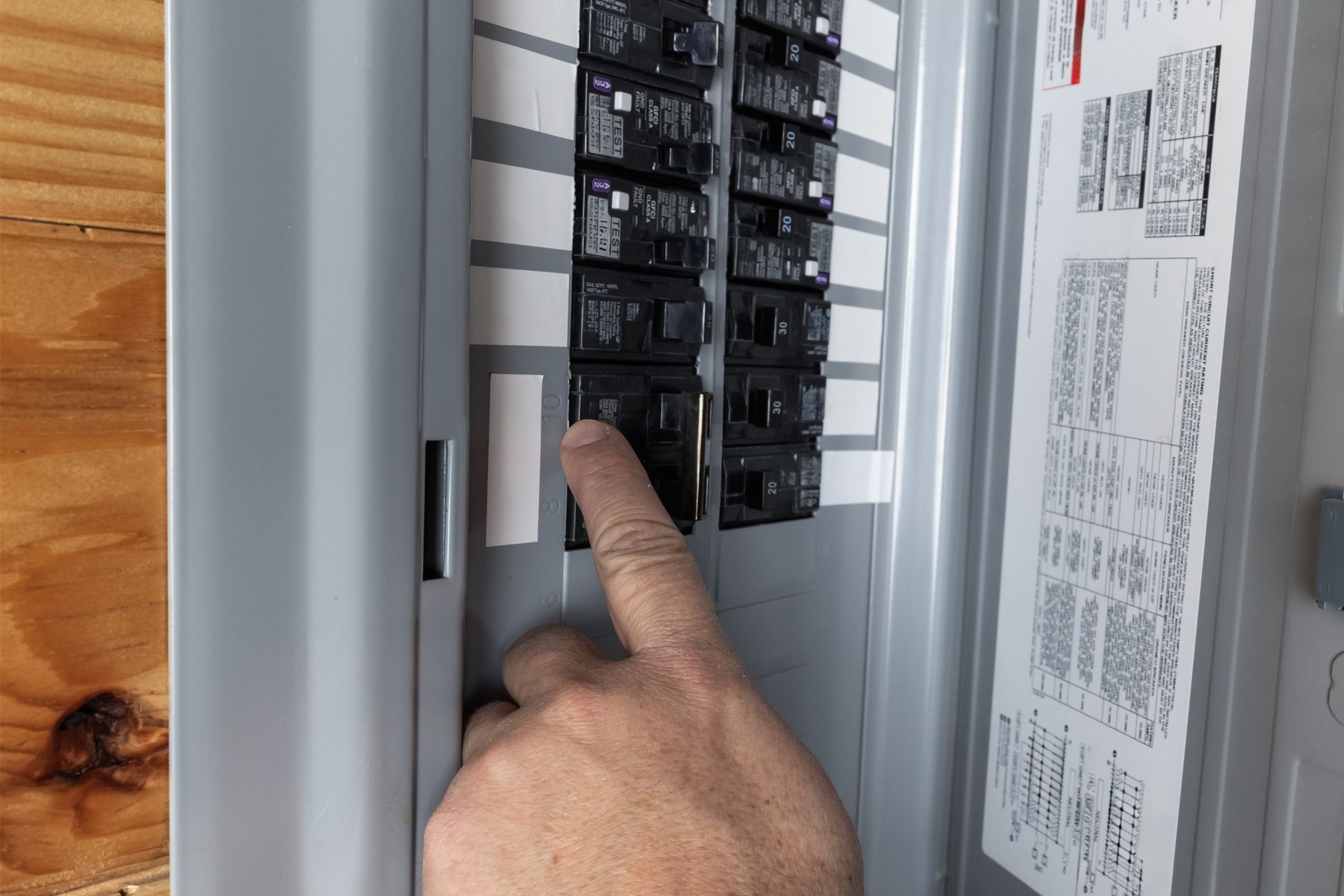 Hand pointing at a circuit breaker panel, with one breaker being pressed.