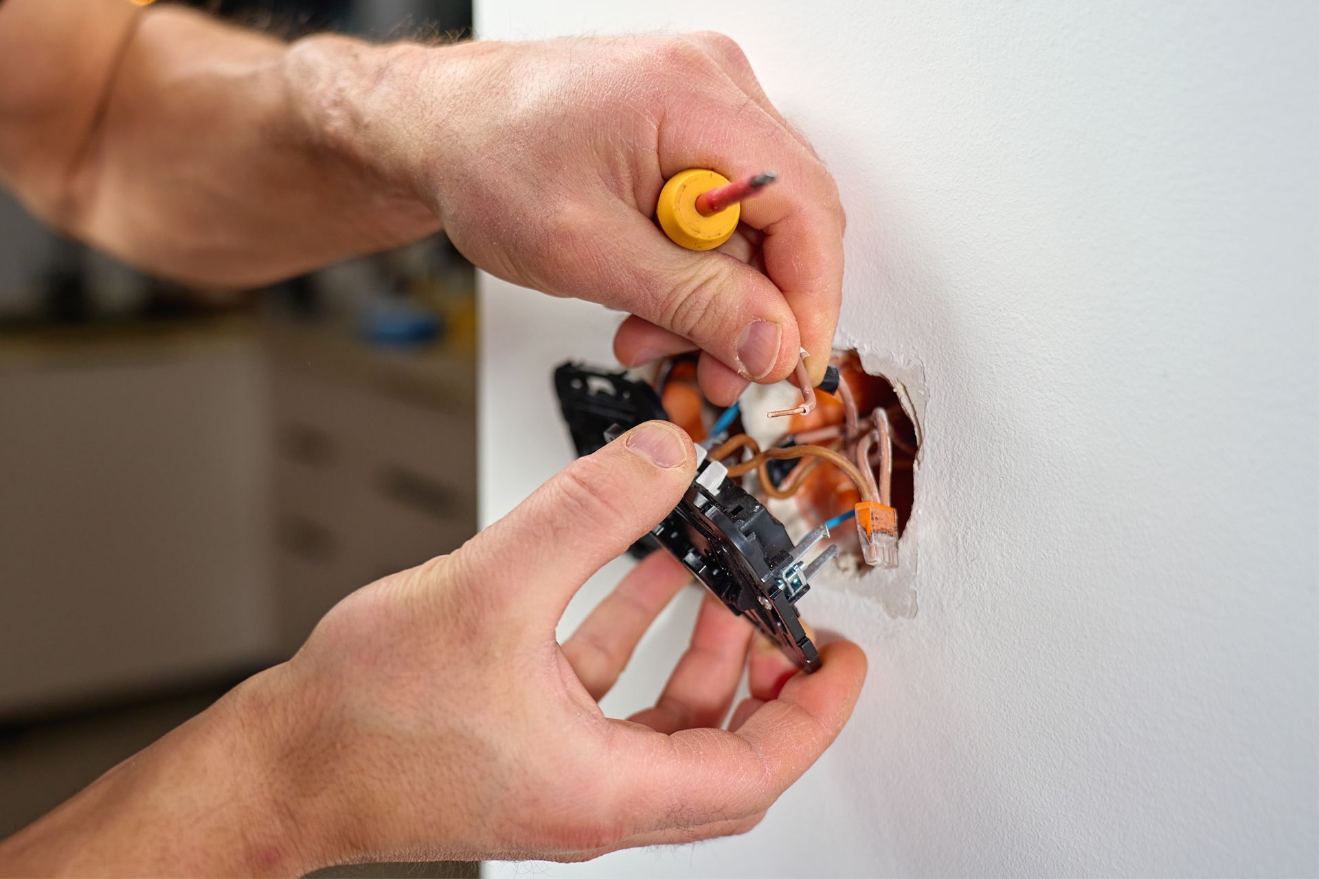Hands repairing a damaged electrical outlet with a screwdriver and exposed wires.