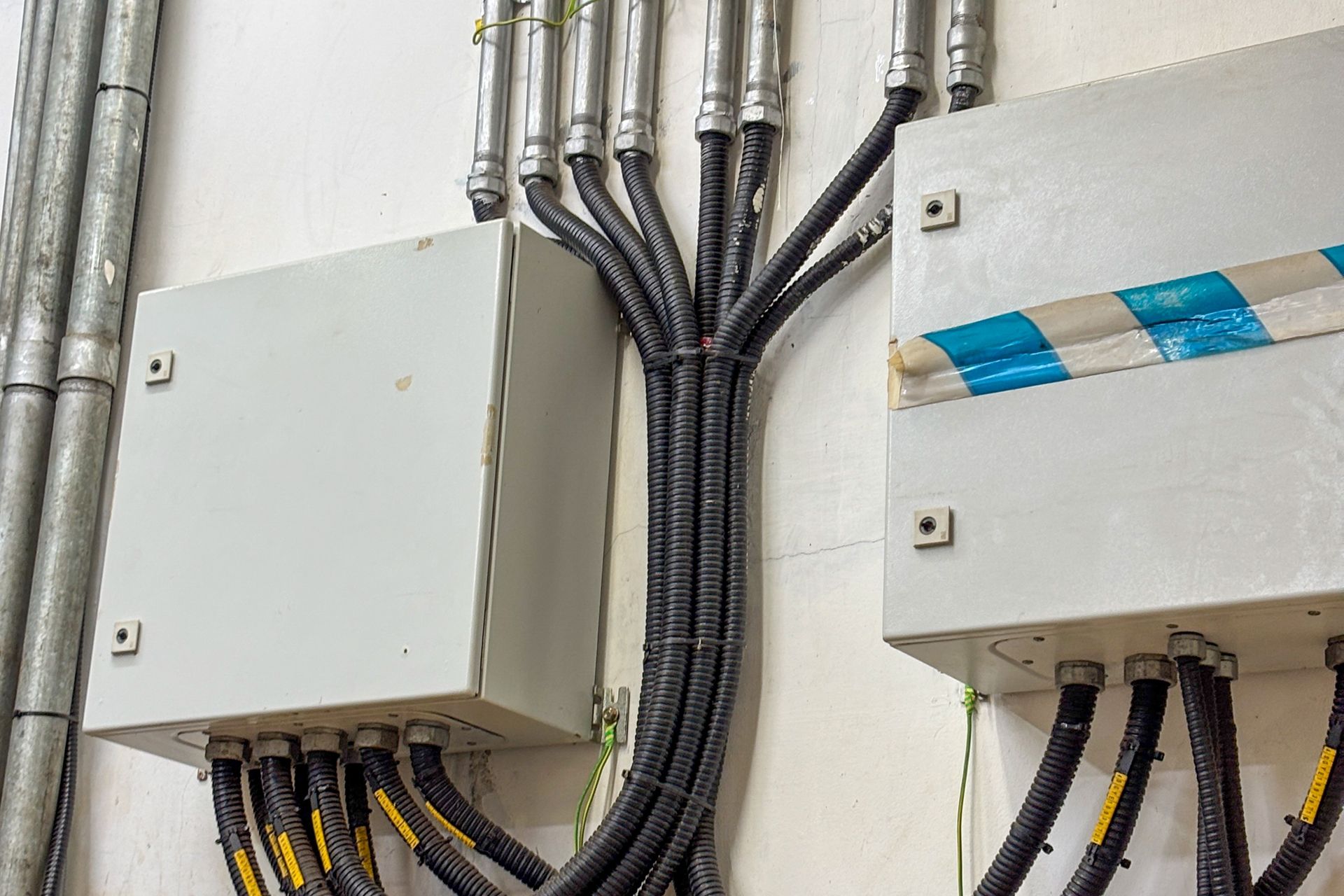 Electrical control boxes with bundled black cables mounted on a wall in an industrial setting.