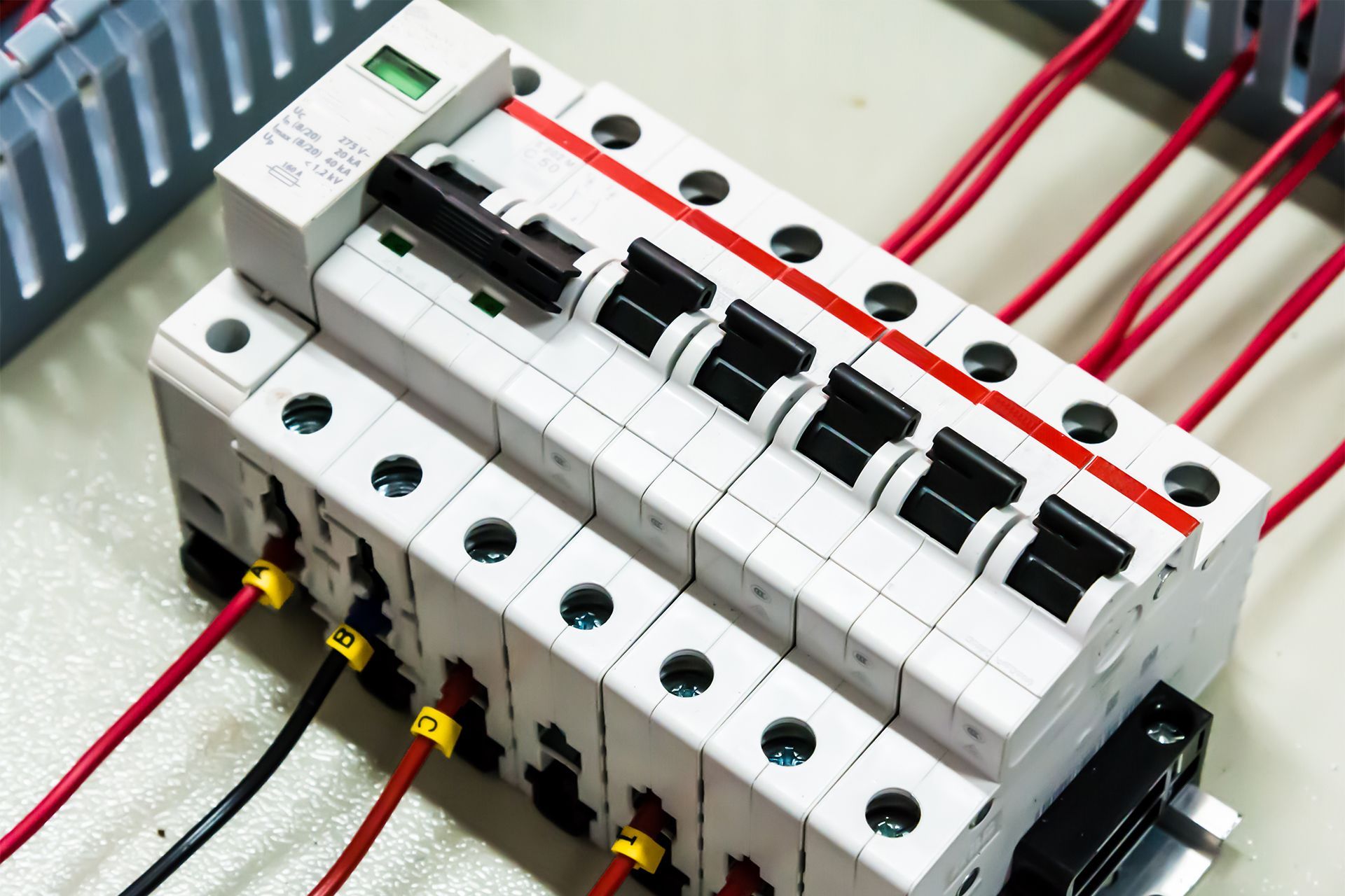 Close-up of a white circuit breaker panel with red wires and black switches on a metal base.