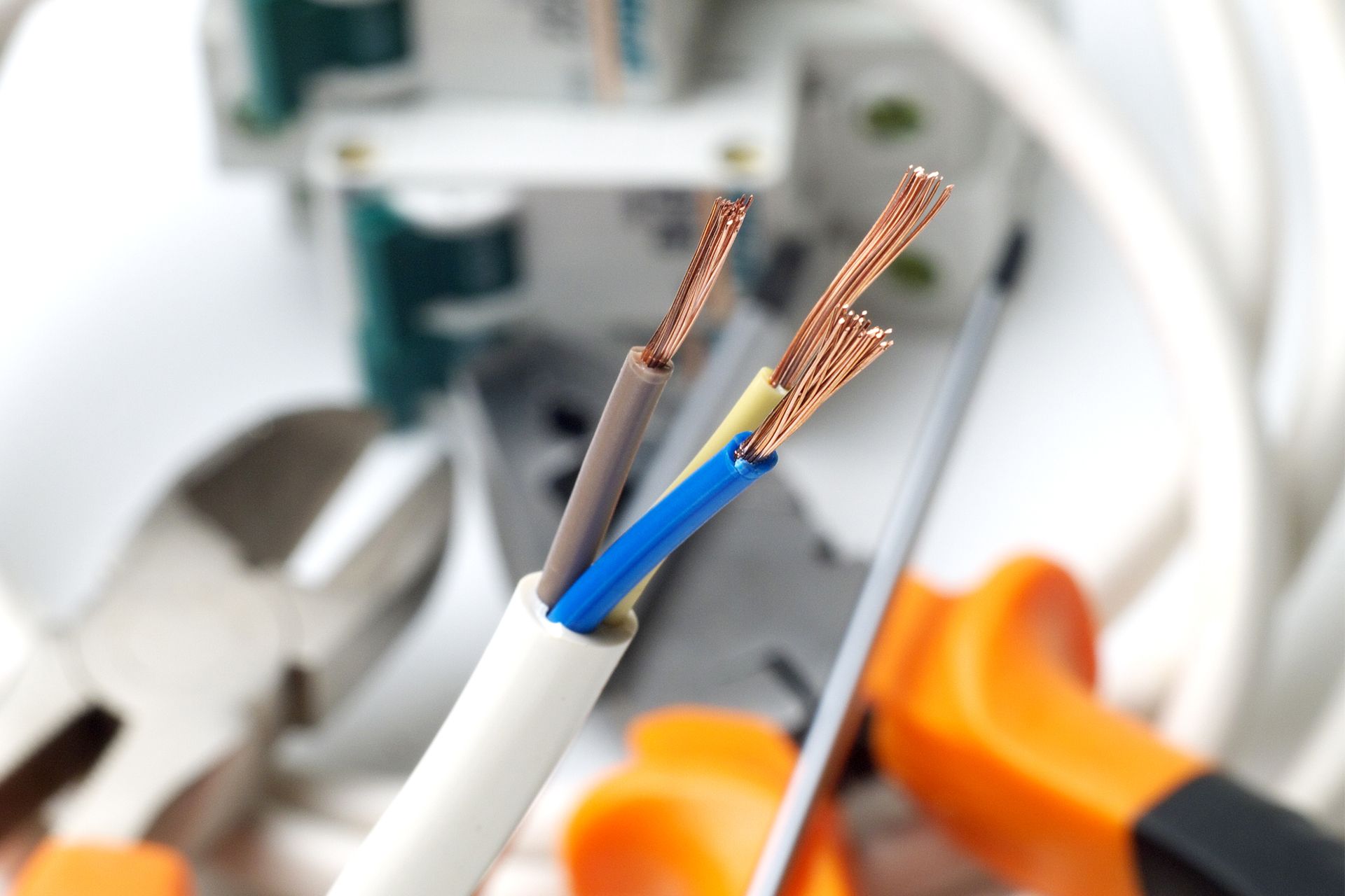 Exposed copper wires in a white cable, with orange tools blurred in the background.