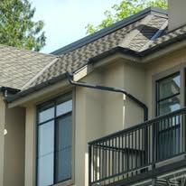 Gloved hands installing a gray gutter on a shingled roof edge