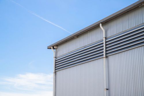 Silver industrial building wall with vents and a gutter against a blue sky