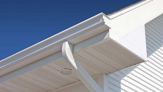 Close-up of a white house roof with gutter, soffit vents, and blue sky