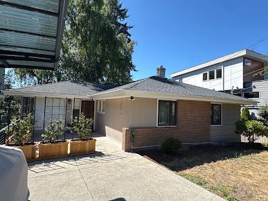 Single-story suburban house with brick and beige exterior, driveway, and small front garden under a clear blue sky