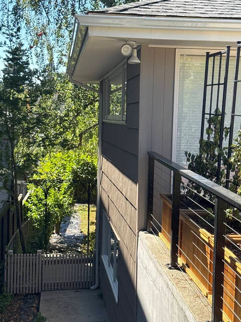 Balcony with black railing beside a house, overlooking a fenced garden and tall trees