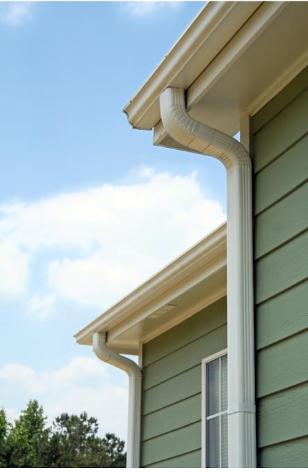 Green house exterior with white trim and gutters against a blue sky