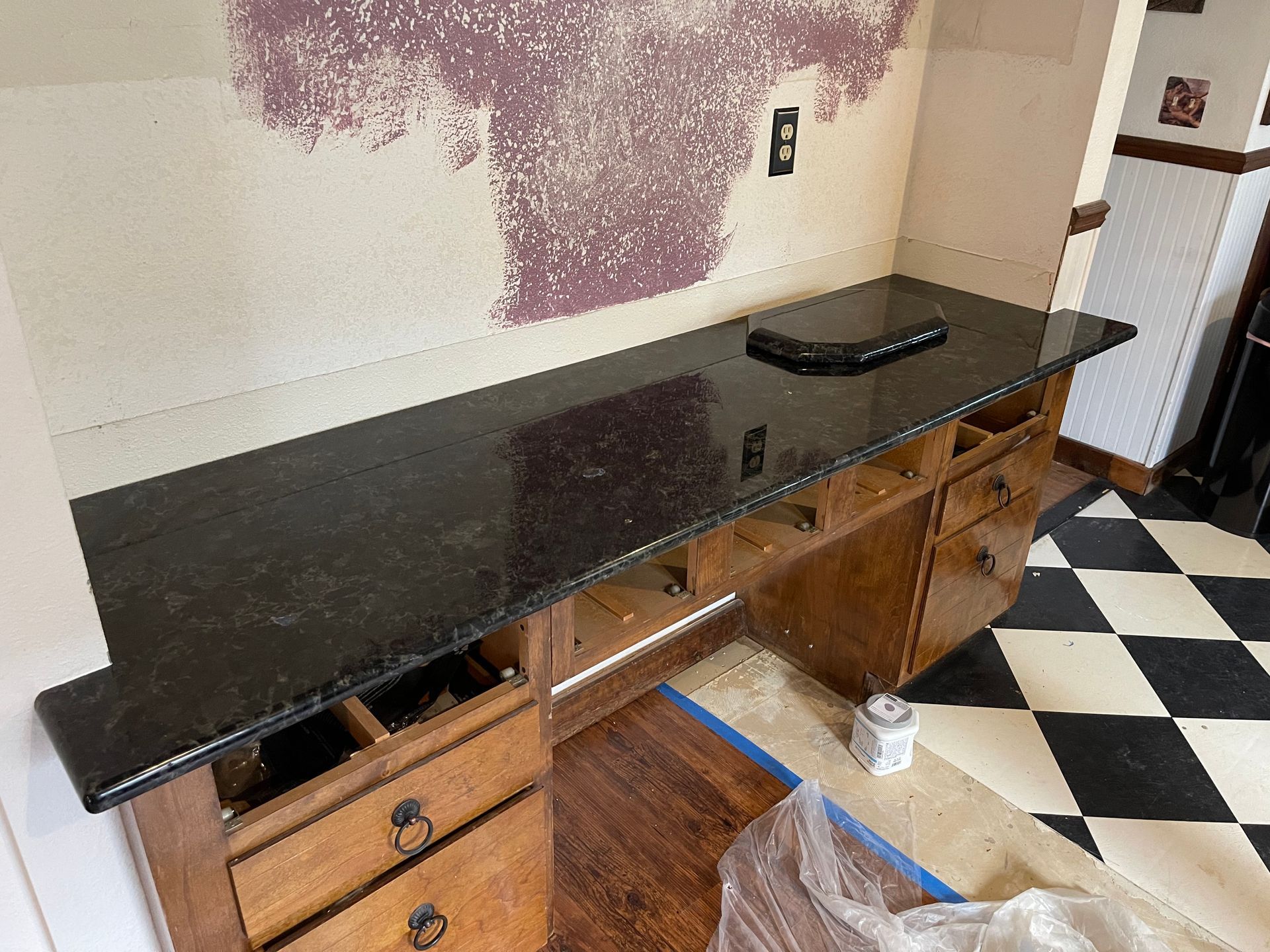 Black countertop on a wooden cabinet in a room with black-and-white checkered floor and peeling wall paint