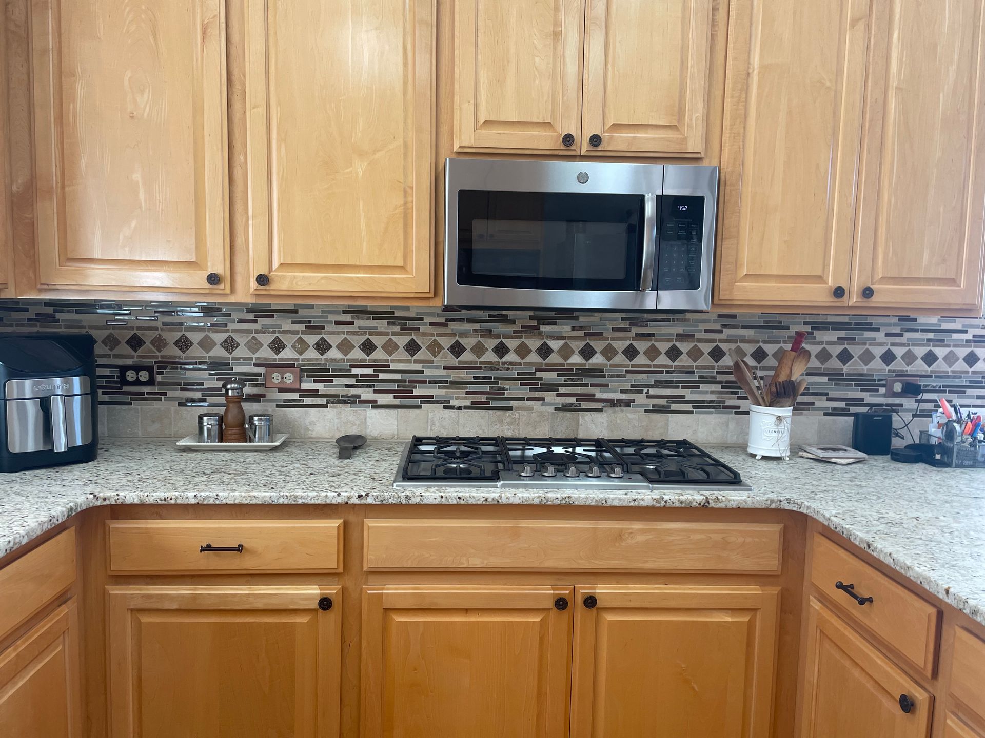 Modern kitchen with wood cabinets, granite counters, stainless microwave, gas stove, and mosaic backsplash