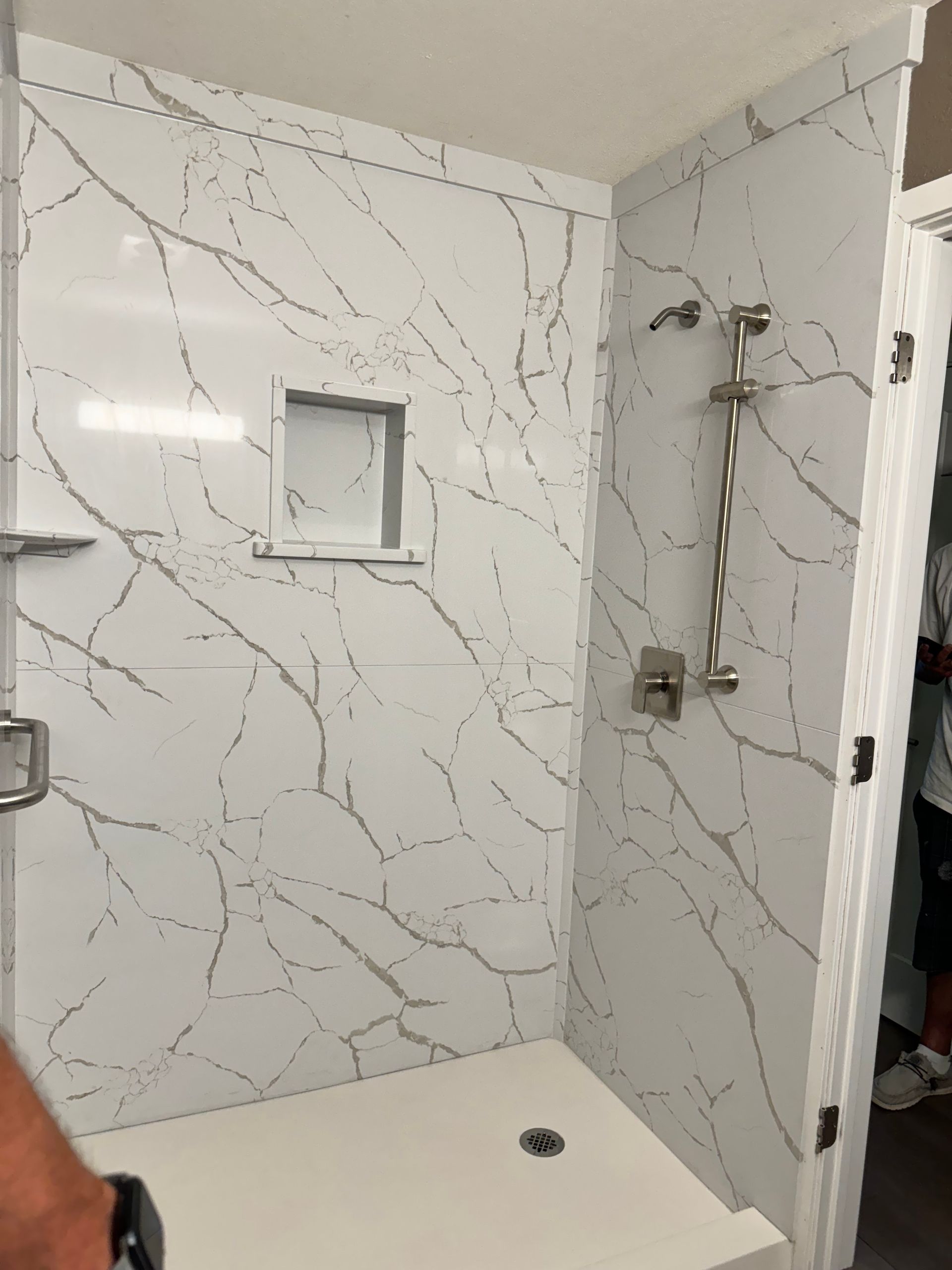 Empty tiled shower with recessed niche and chrome showerhead, viewed from inside.