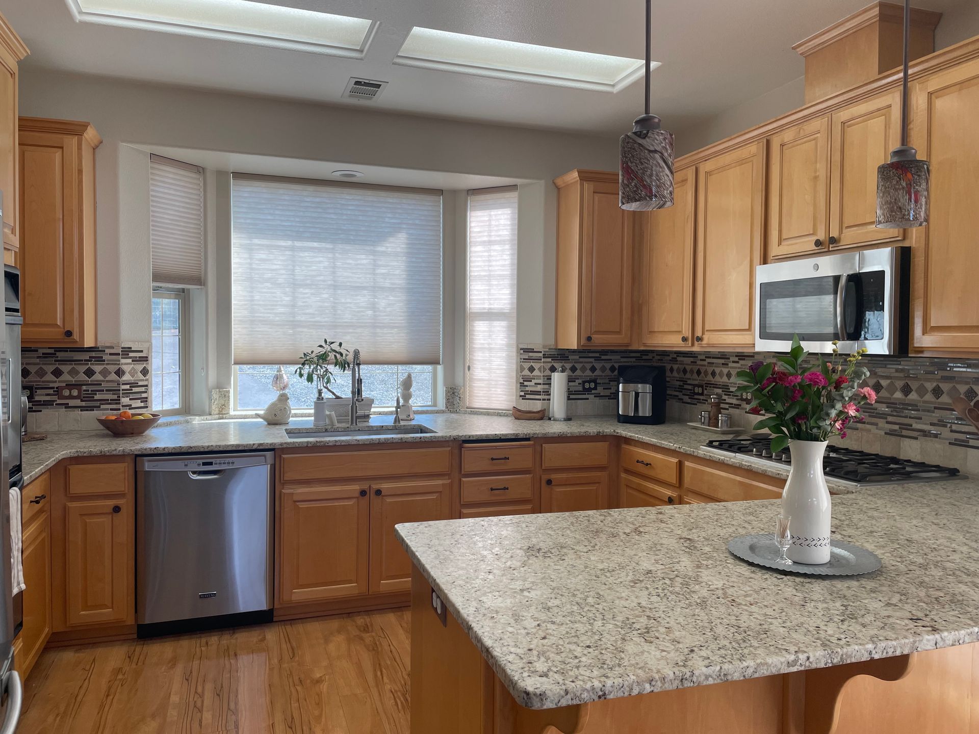 Bright kitchen with wood cabinets, granite island, stainless appliances, and a window over the sink.