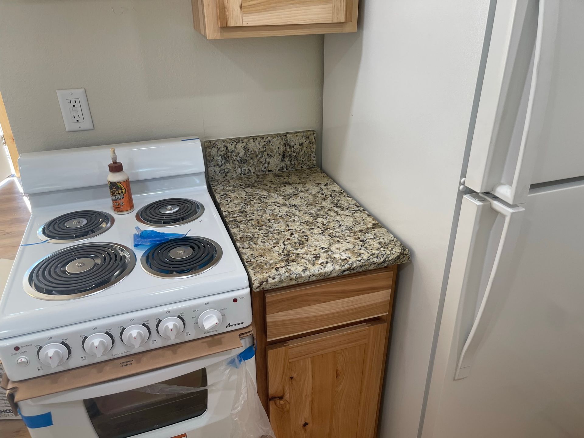 Small kitchen corner with white stove, granite countertop, wooden cabinet, and white refrigerator