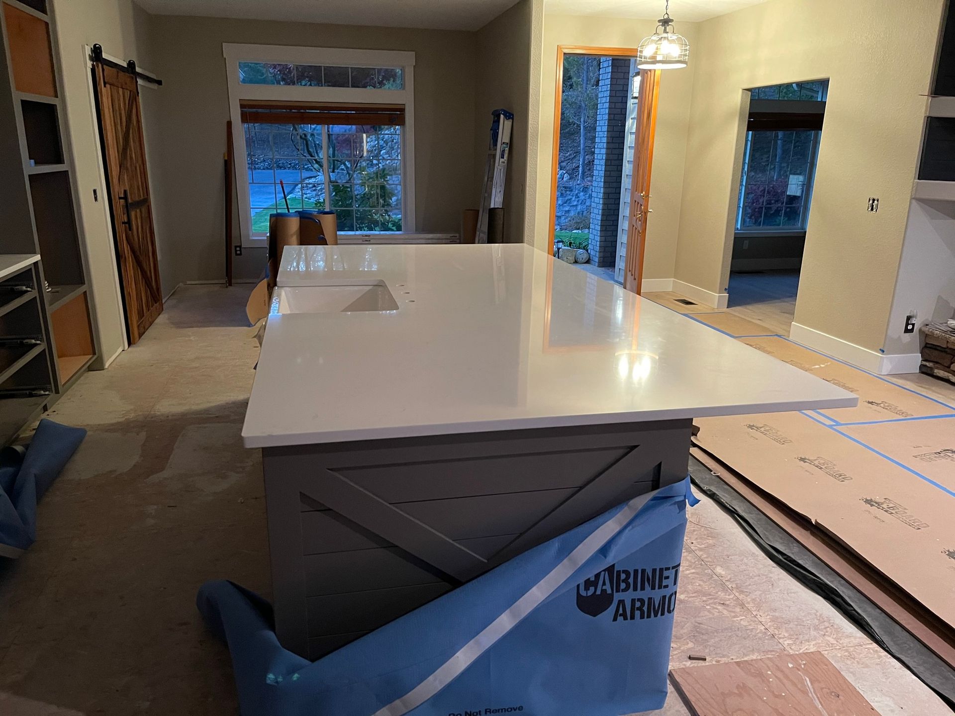 Kitchen under construction with white island countertop, open cabinets, and flooring materials on the floor