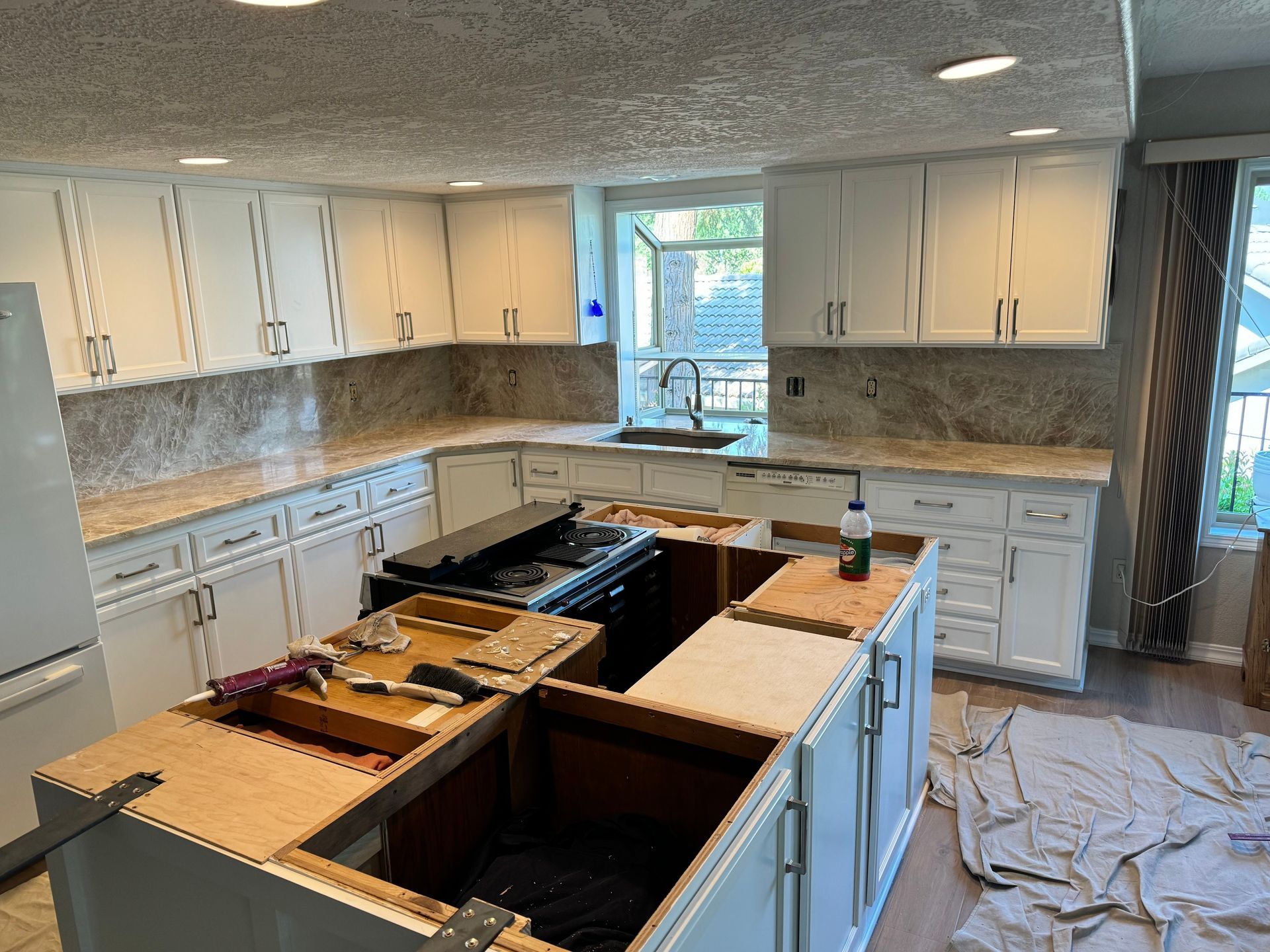 Partially renovated kitchen with white cabinets, granite counters, and an island under construction
