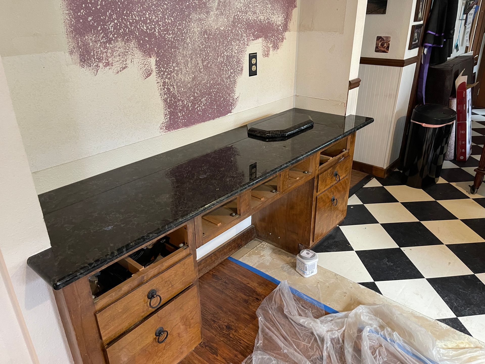 Black countertop cabinet in a kitchen under renovation, with open drawers and checkered tile floor