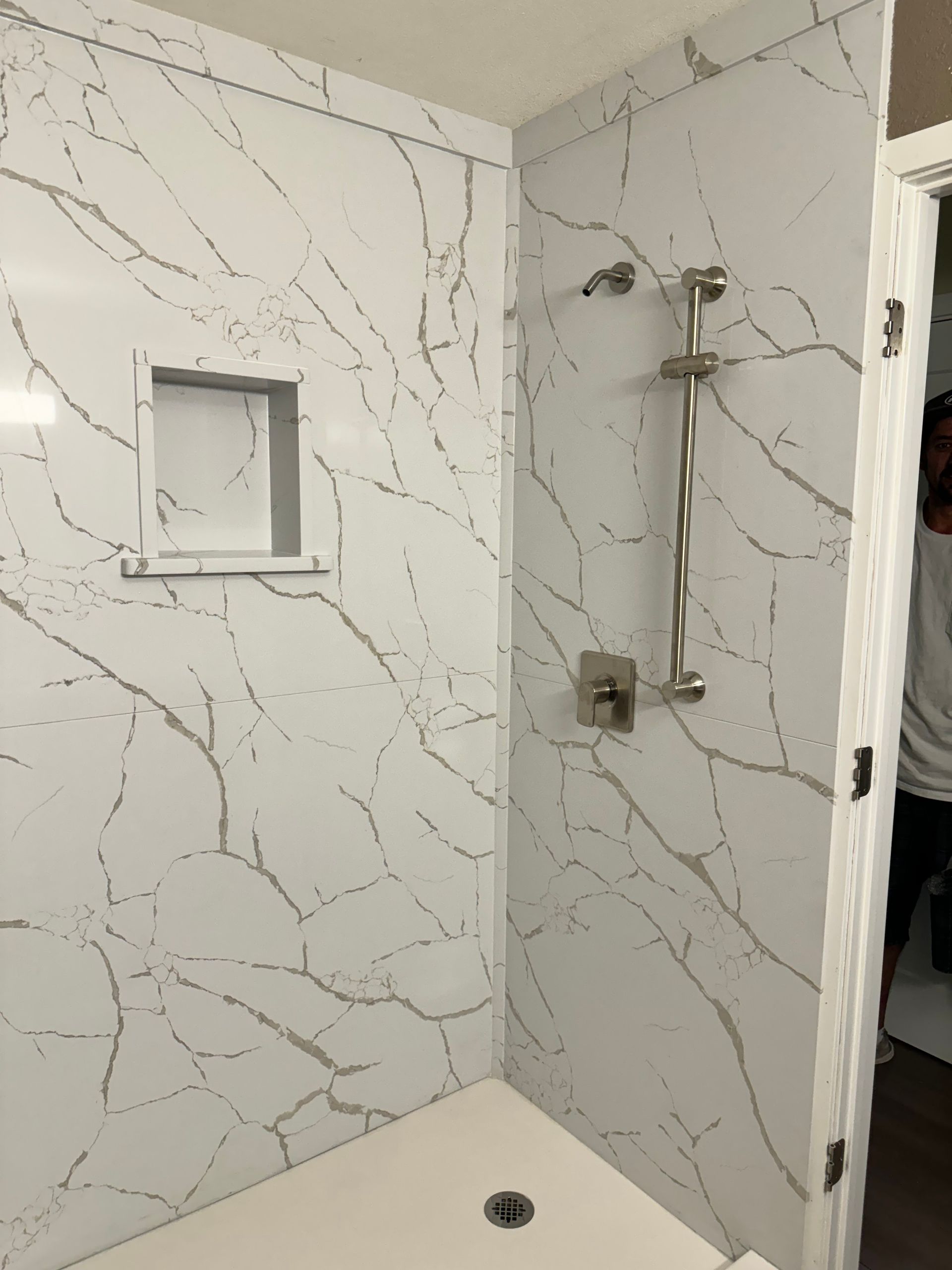 White marble-look shower with built-in shelf and showerhead in a tiled bathroom corner