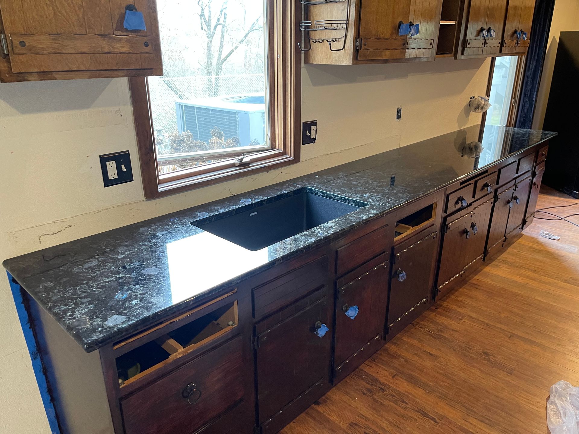 Kitchen counter with dark granite top, sink, and wooden cabinets beneath a window.
