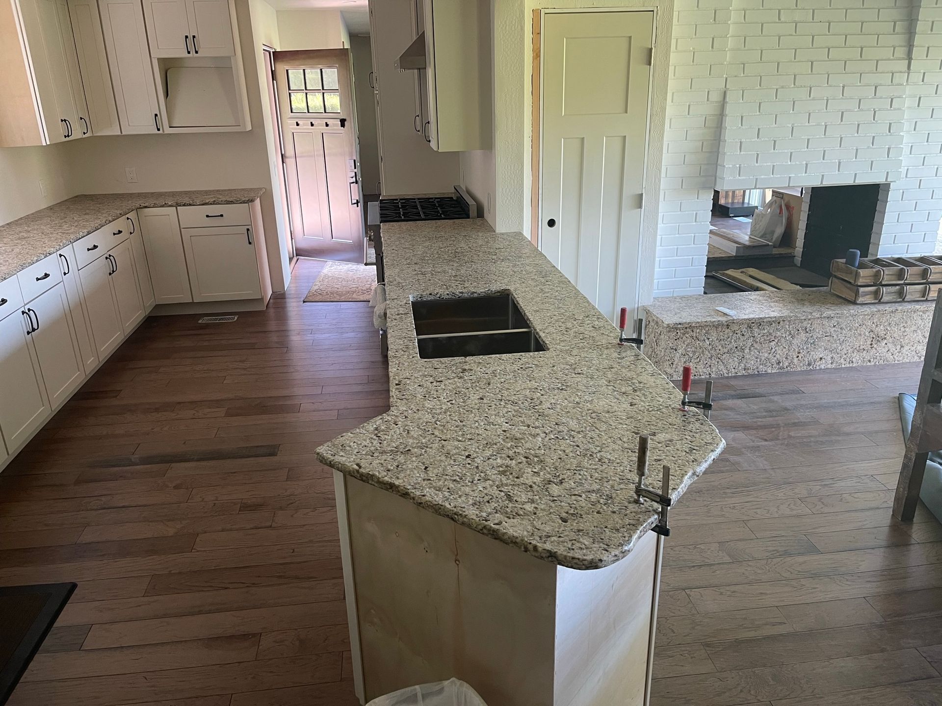 Spacious kitchen with white cabinets, granite island, hardwood floors, and a stone fireplace in the adjoining room