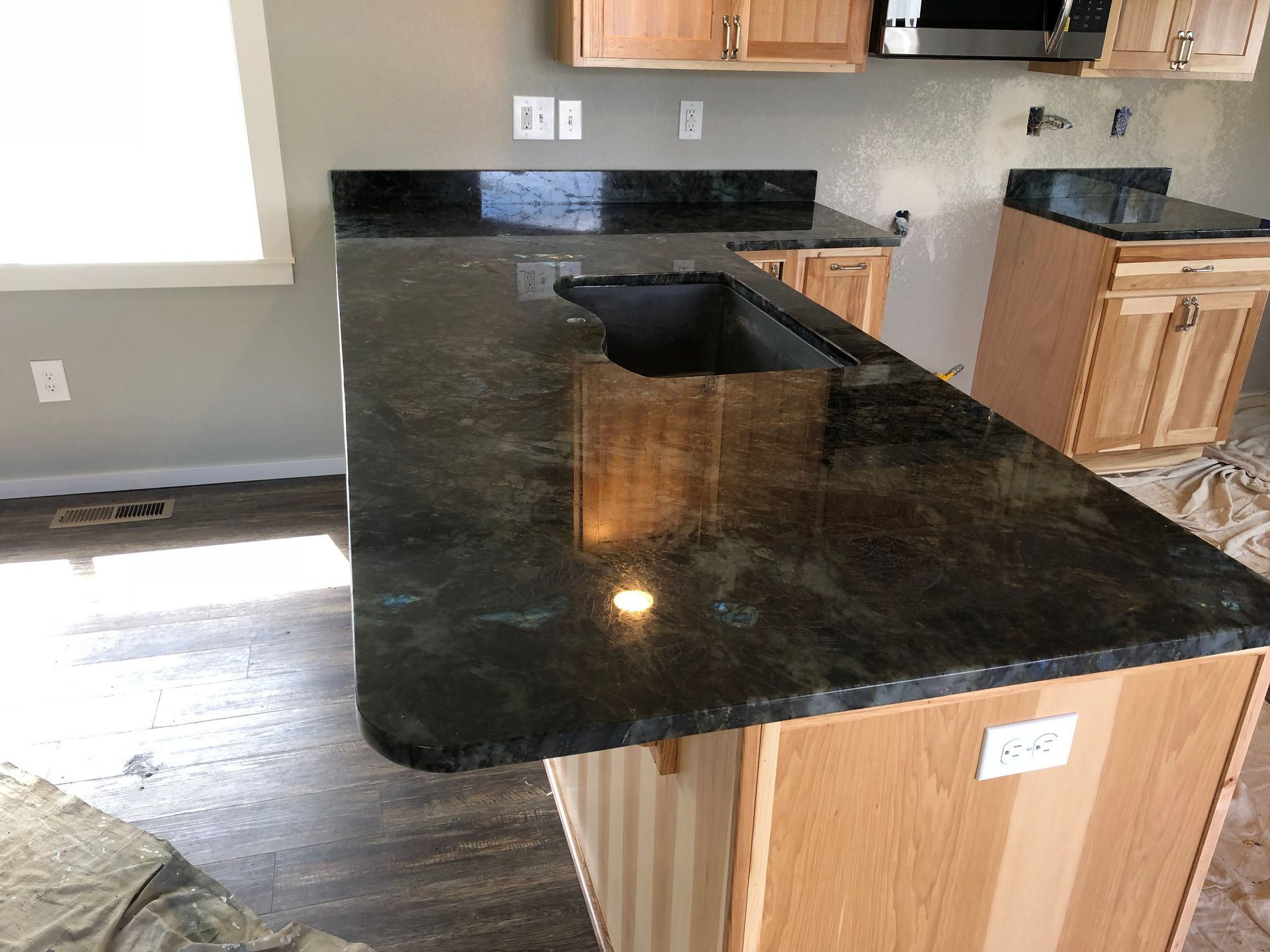 Kitchen with dark granite island countertop and sink, light wood cabinets, and wood flooring