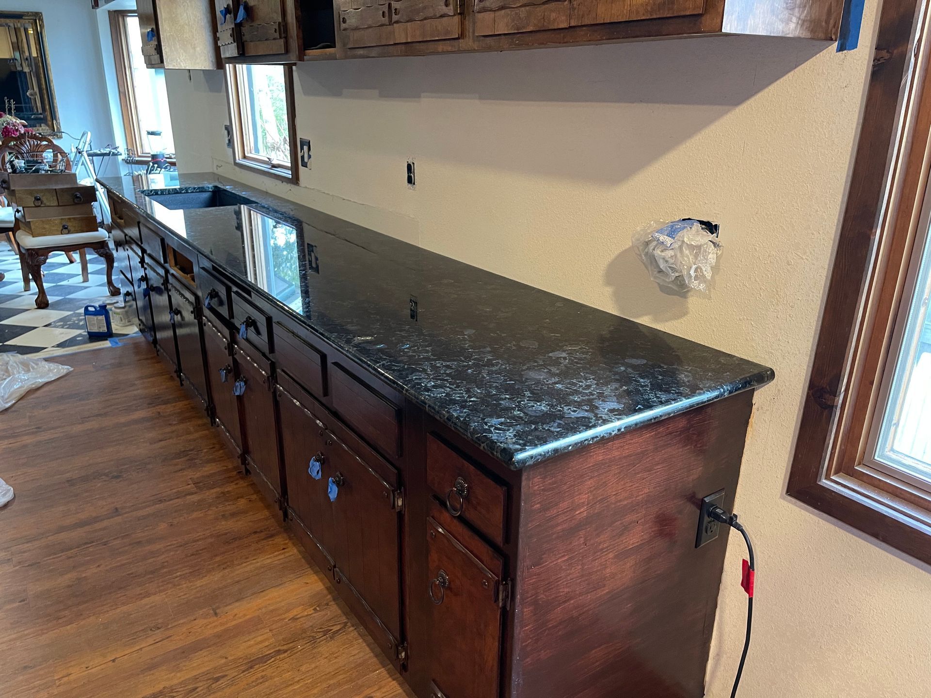Granite-topped dark wood cabinets and drawers along a kitchen wall, with wood floor and window light