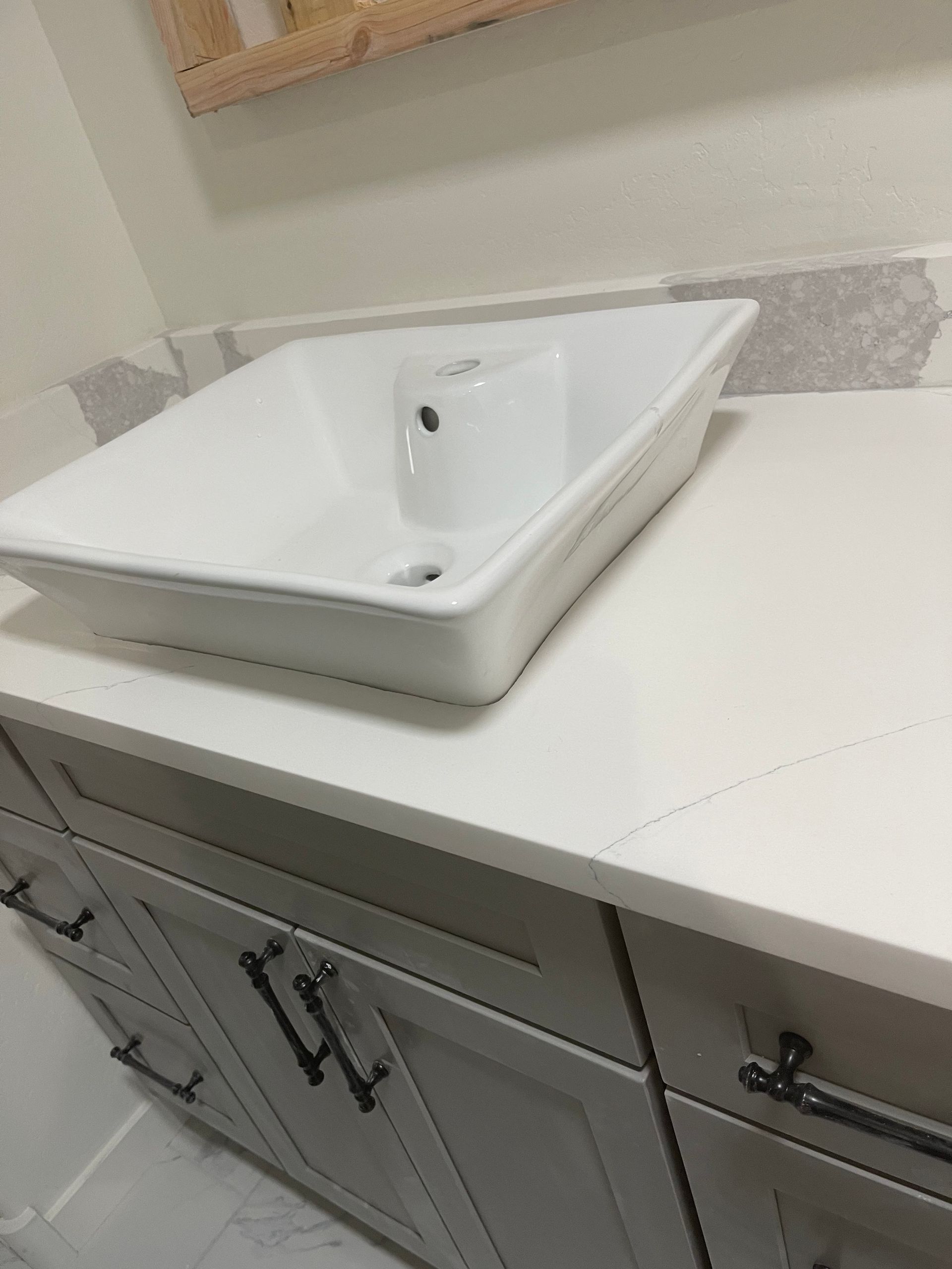 White bathroom sink on a speckled countertop above light wood cabinets and tiled floor