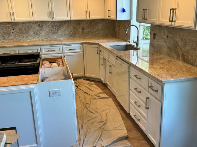 Kitchen under renovation with cabinets, countertops, tarp-covered floor, and an open dishwasher.