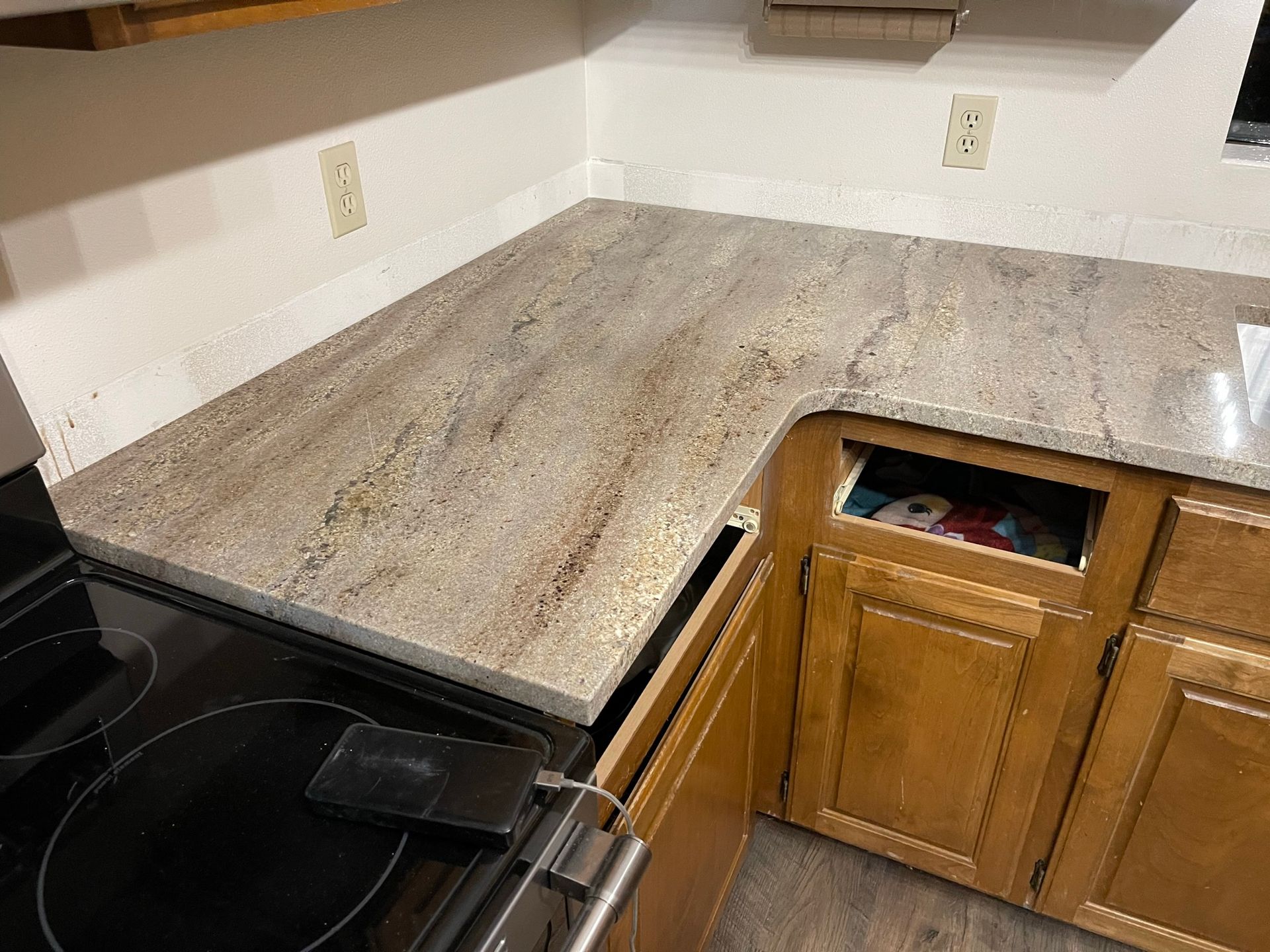 Kitchen countertop with granite surface, wooden cabinets, and a black stovetop in the corner.