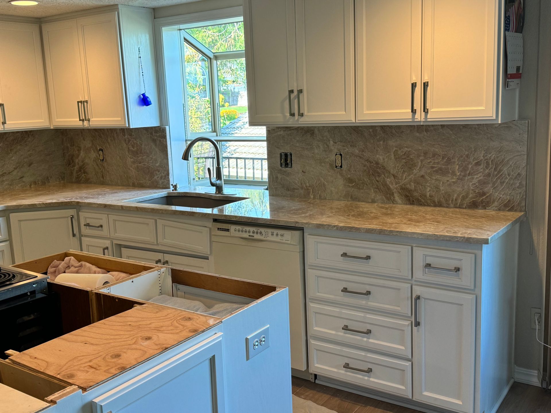 Kitchen under renovation with cream cabinets, marble-look countertops, and an open cabinet drawer in the foreground