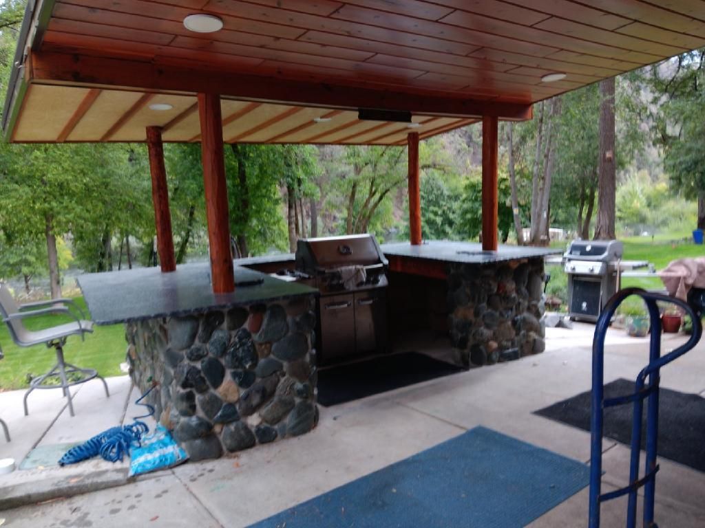 Covered outdoor picnic shelter with stone grilling counter, grill, and picnic table in a wooded park