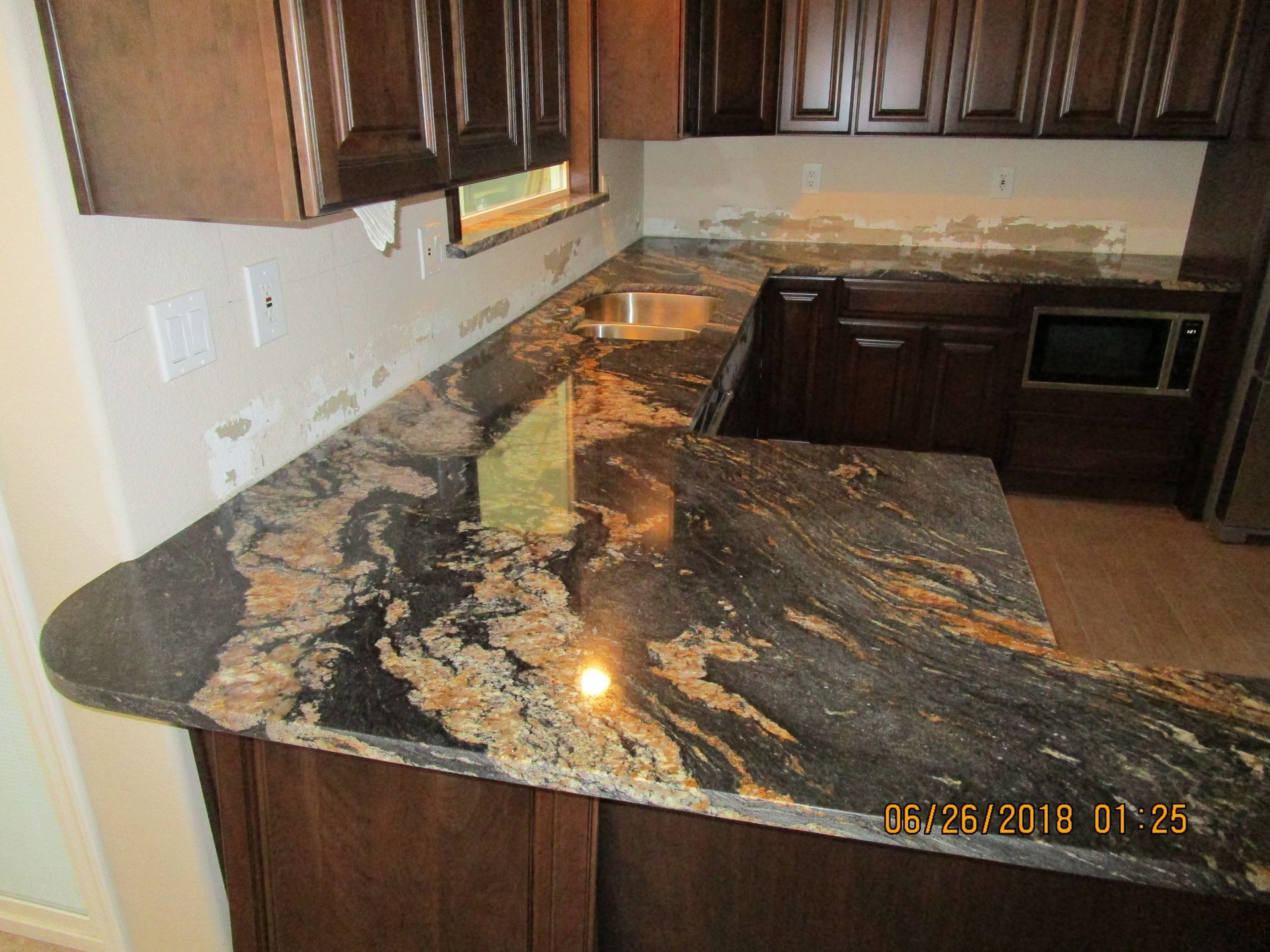 Kitchen with dark wood cabinets and a glossy black-and-gold granite countertop and backsplash.