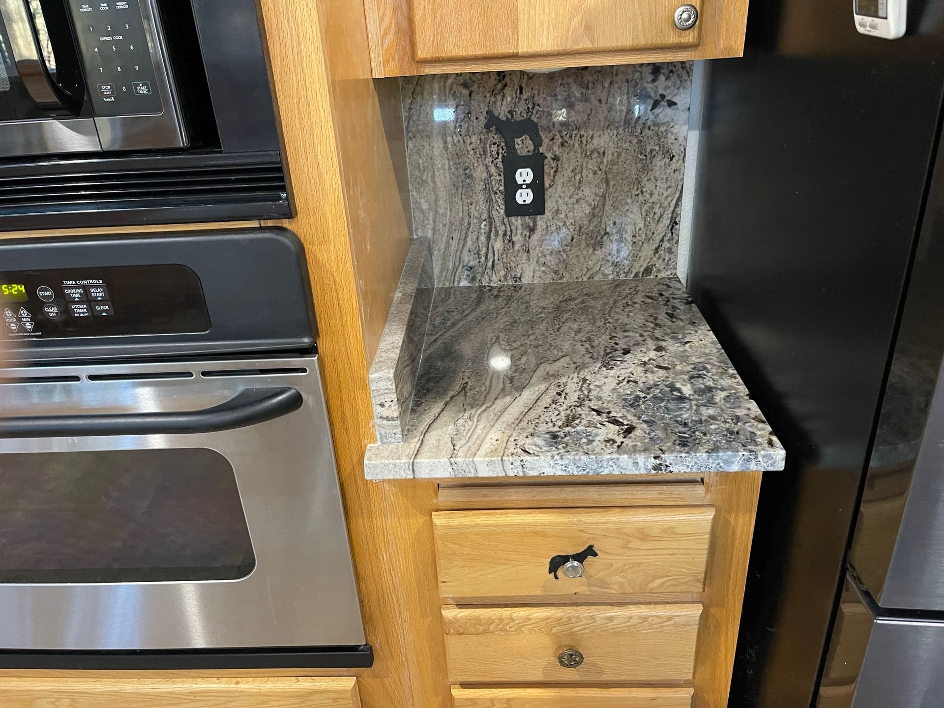 Kitchen nook with granite countertop, wood cabinets, outlet, and stainless steel oven and refrigerator by the counter