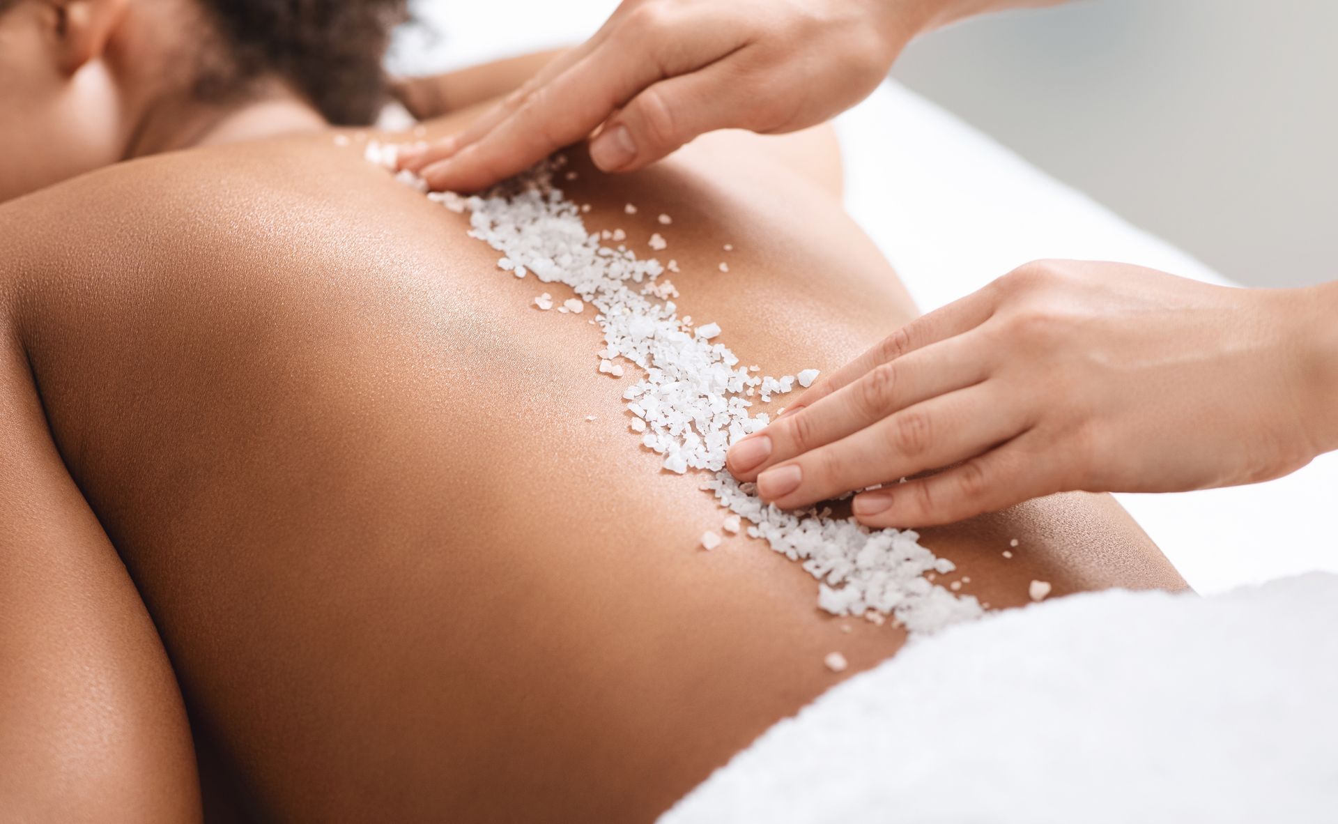 Person receiving a back scrub with white salt crystals during a spa treatment