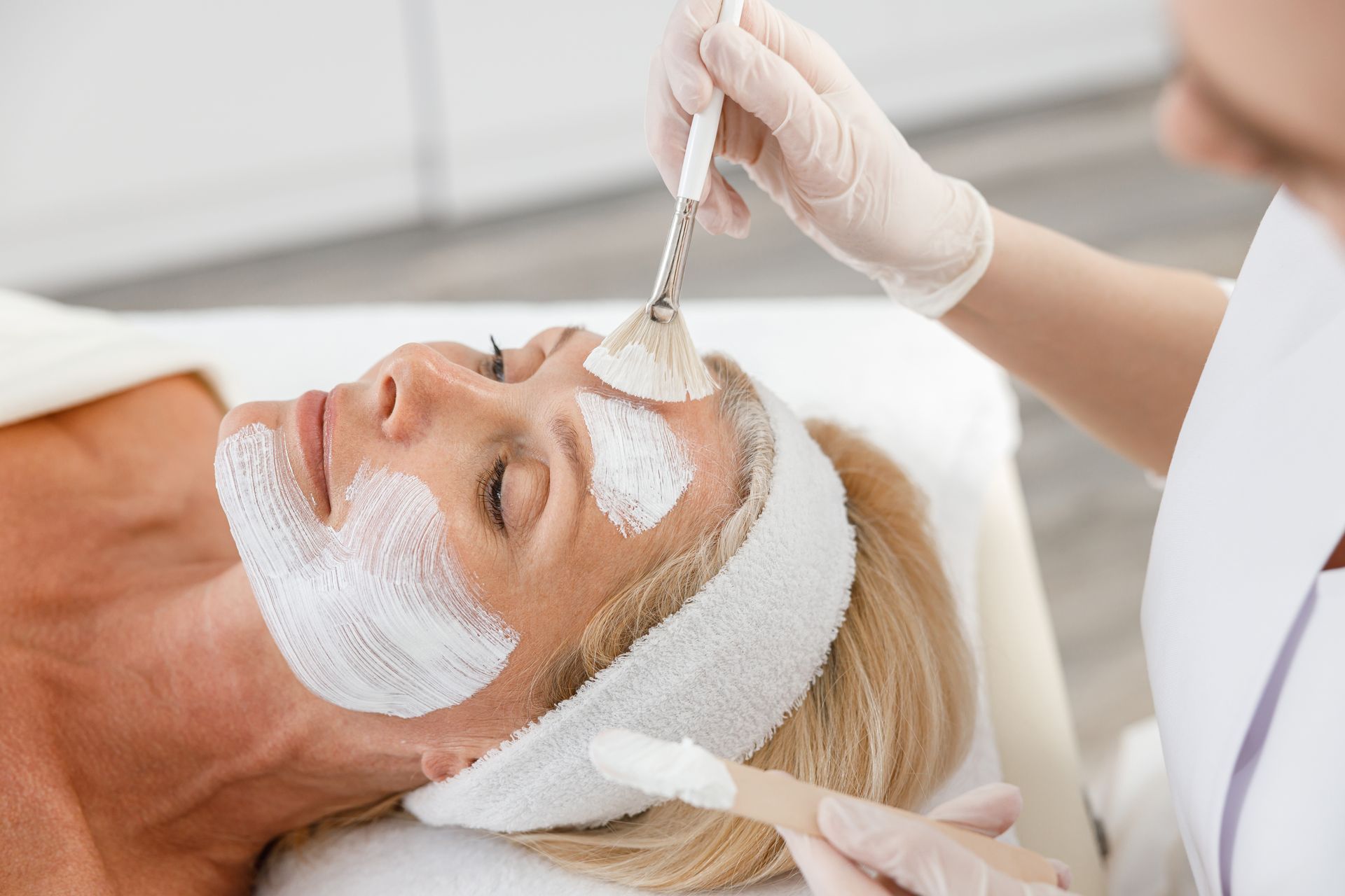 Aesthetic facial treatment with white mask being applied by gloved hands in a spa setting