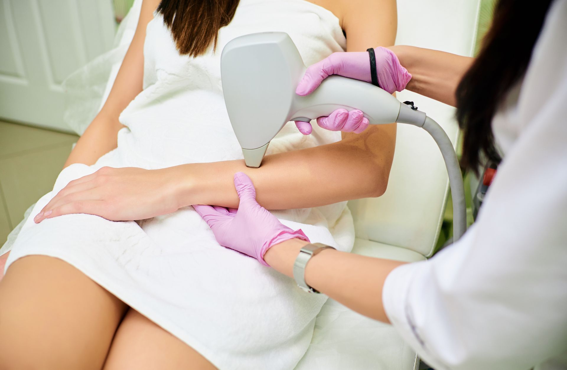 Laser hair removal treatment on a client’s bikini area, with technician wearing pink gloves.