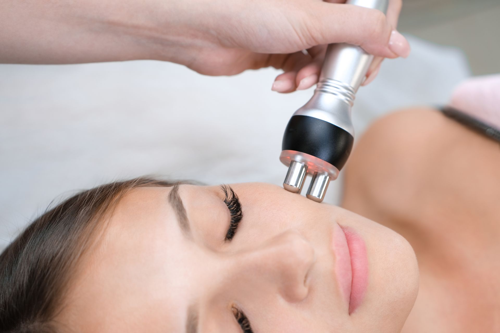 Facial massage device gliding over a woman's cheek during a spa treatment