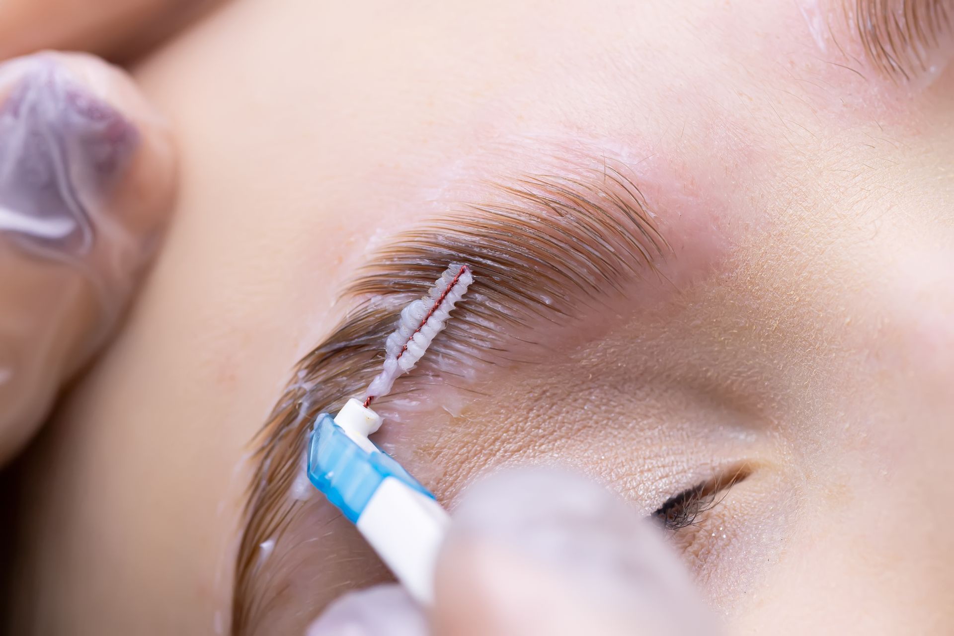 Applying white eyebrow tint with a small brush on a closed eye