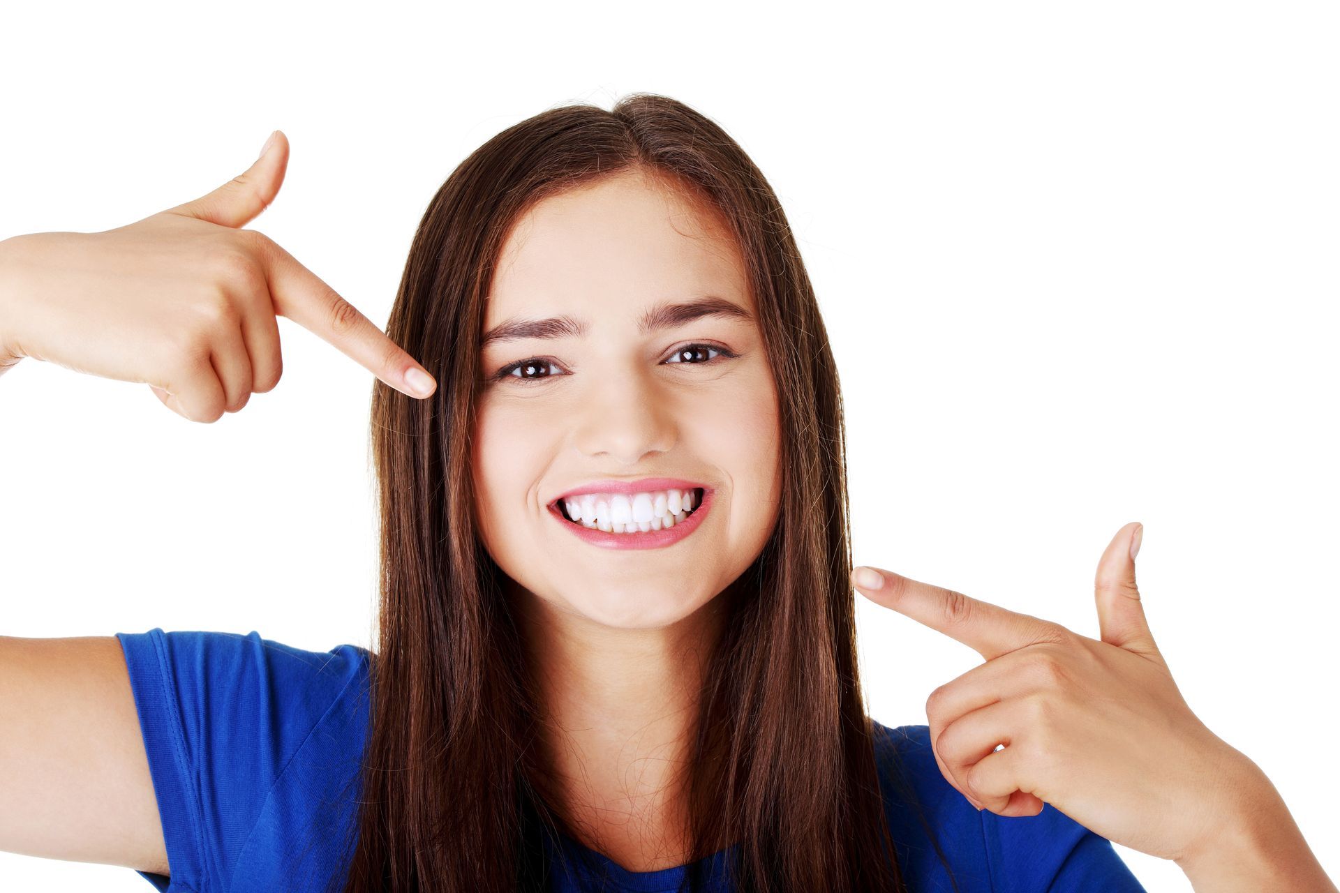 Smiling woman in blue shirt pointing at her teeth with both hands on a white background