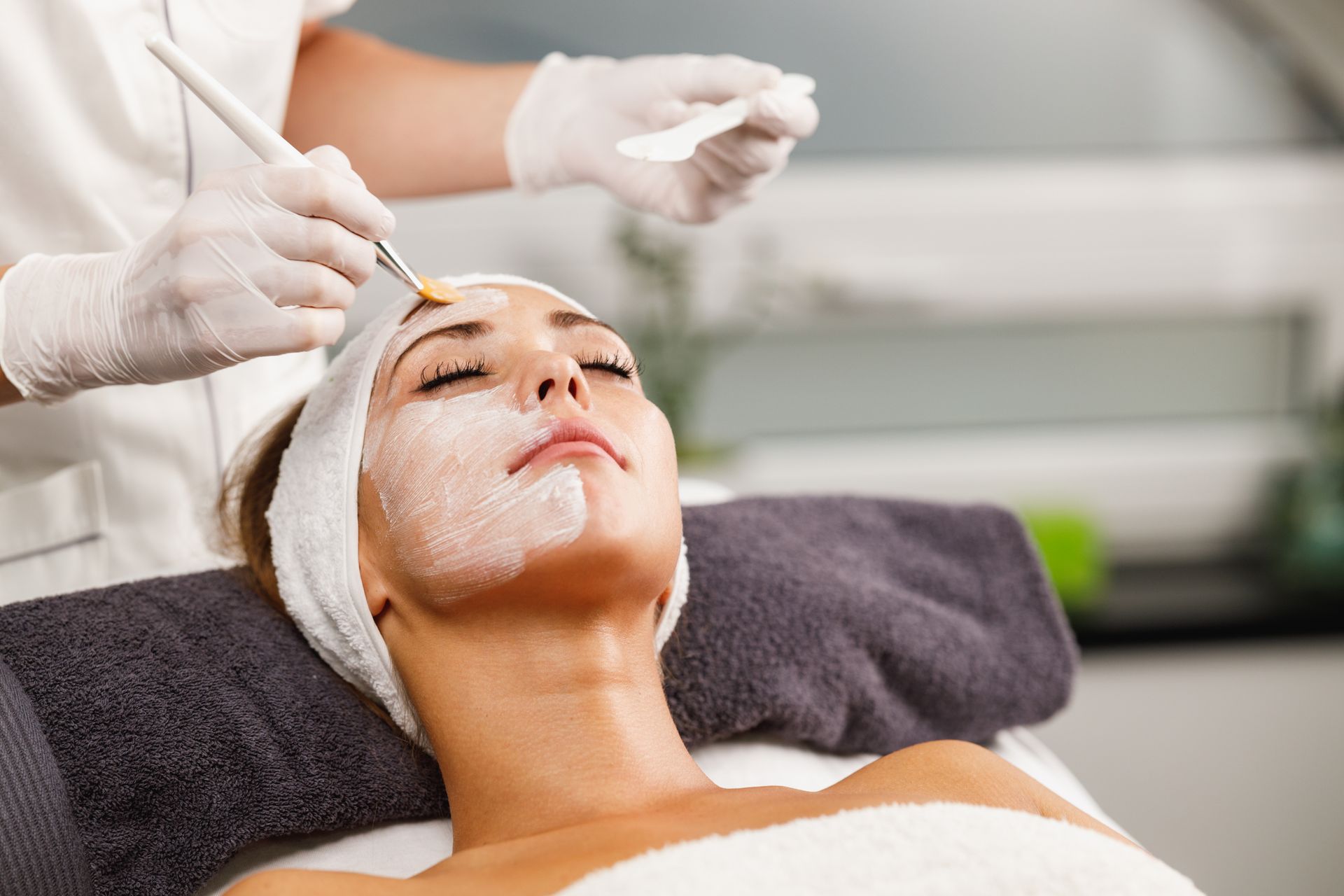 Facial treatment in progress as gloved esthetician applies product to a client’s face using a brush