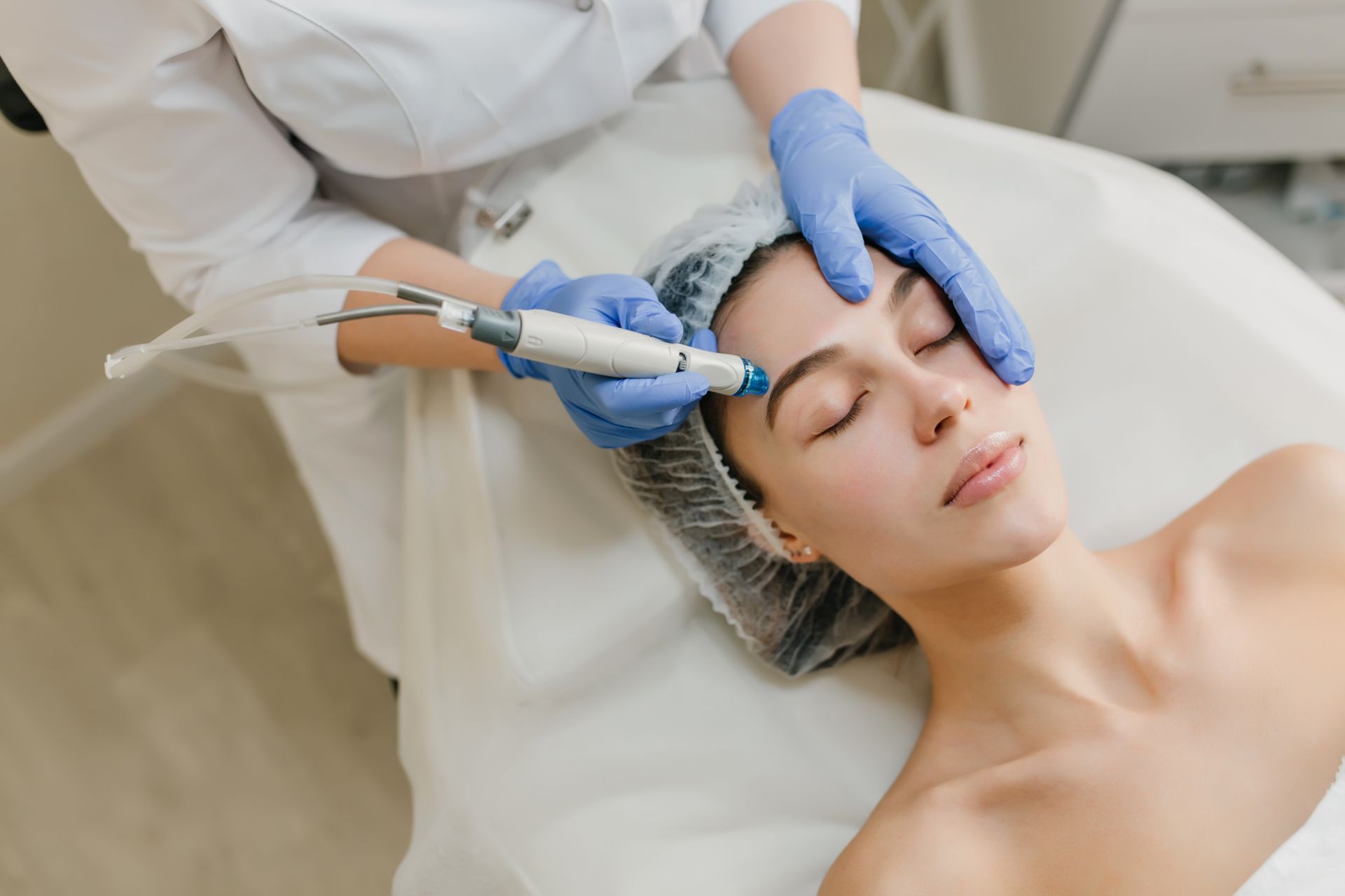 Aesthetic treatment on a woman’s face with a gloved clinician holding a handheld device and her forehead