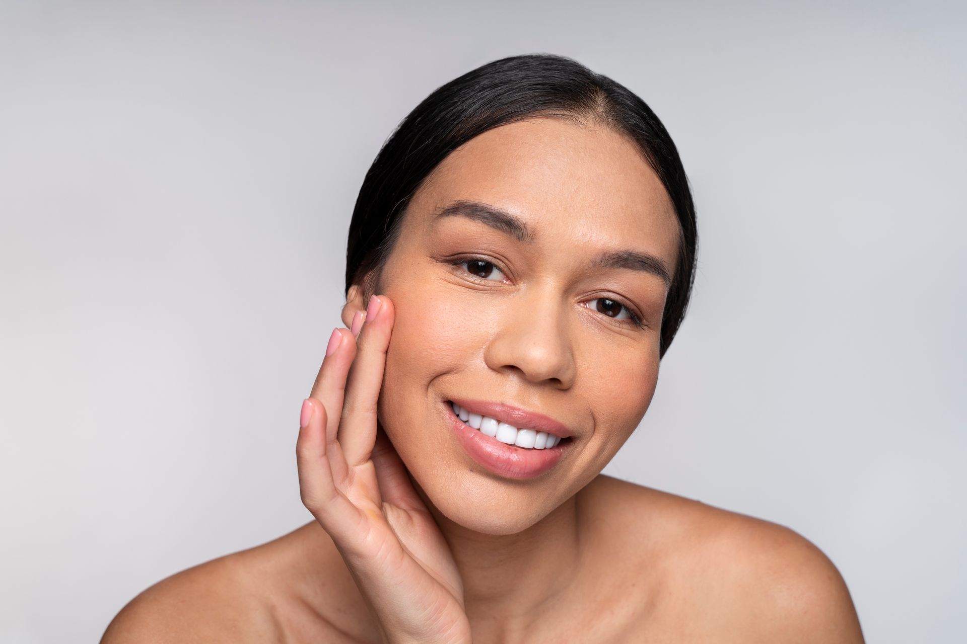a woman is smiling and touching her face with her hand .