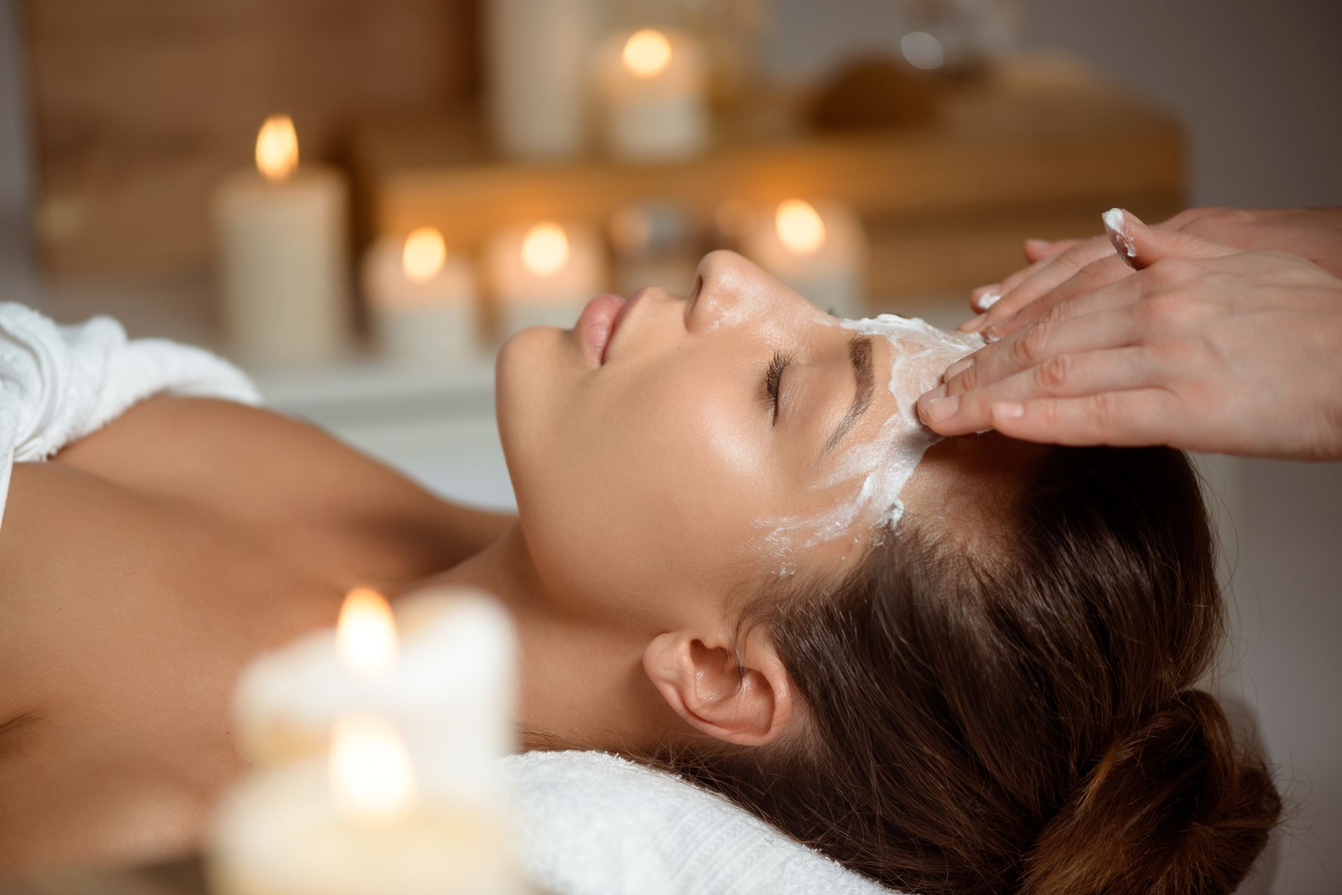 Woman receiving facial treatment in spa, candles lit, eyes closed.